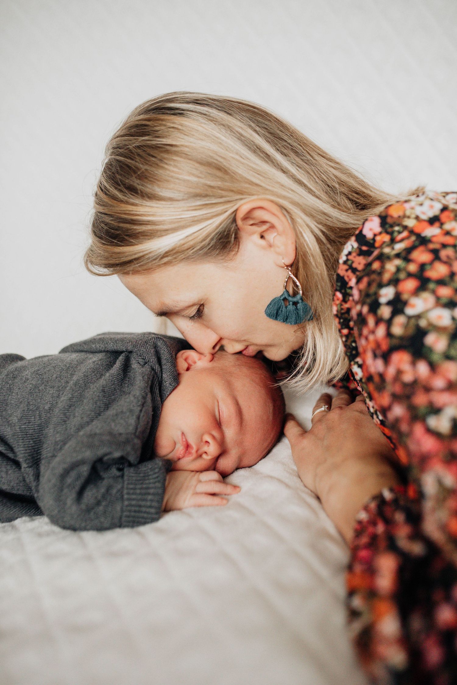 Parent in floral dress sharing sweet close-up moments with child on light bedding.