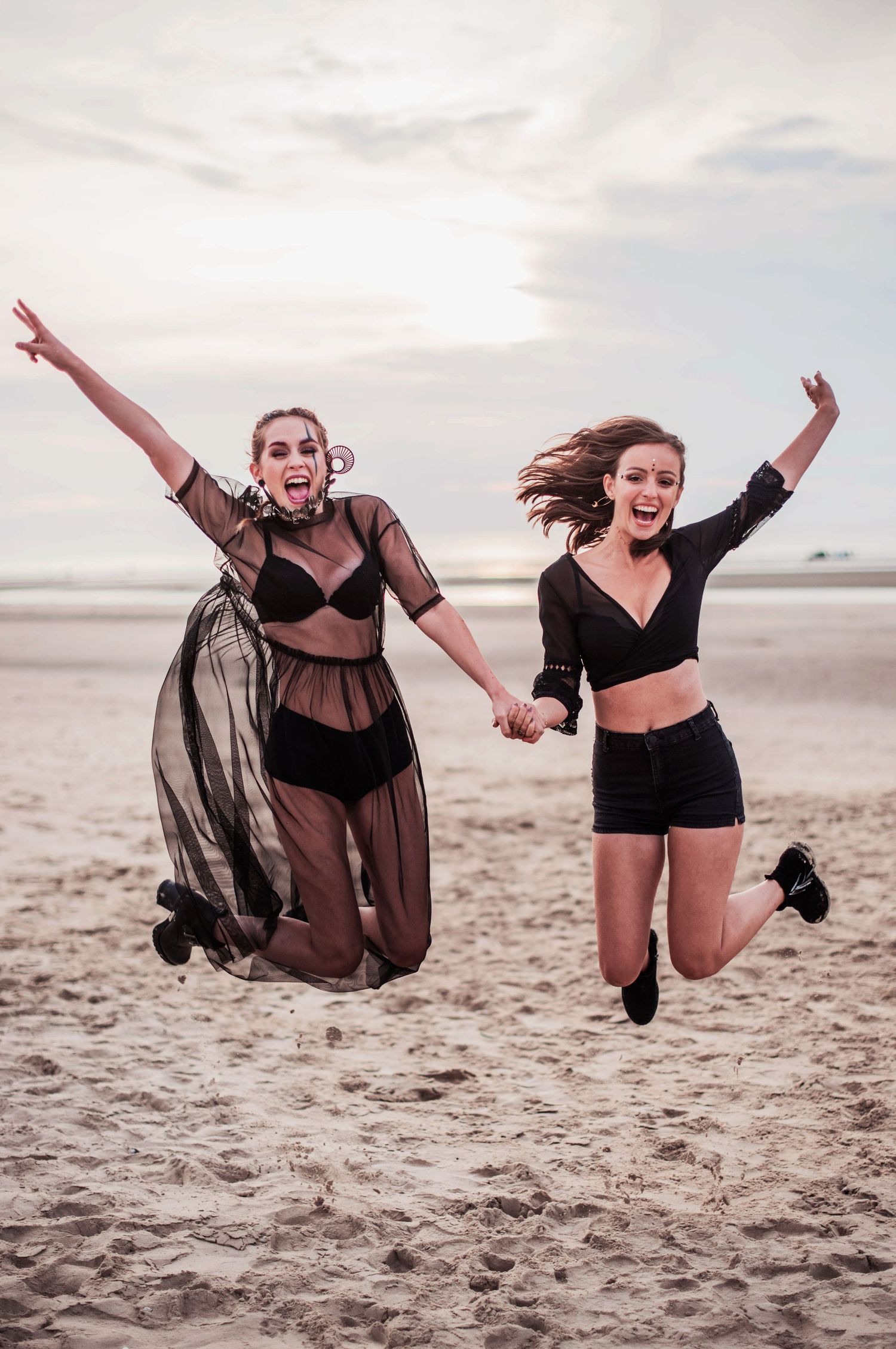 Friends jumping joyfully on the beach at sunset wearing black outfits.