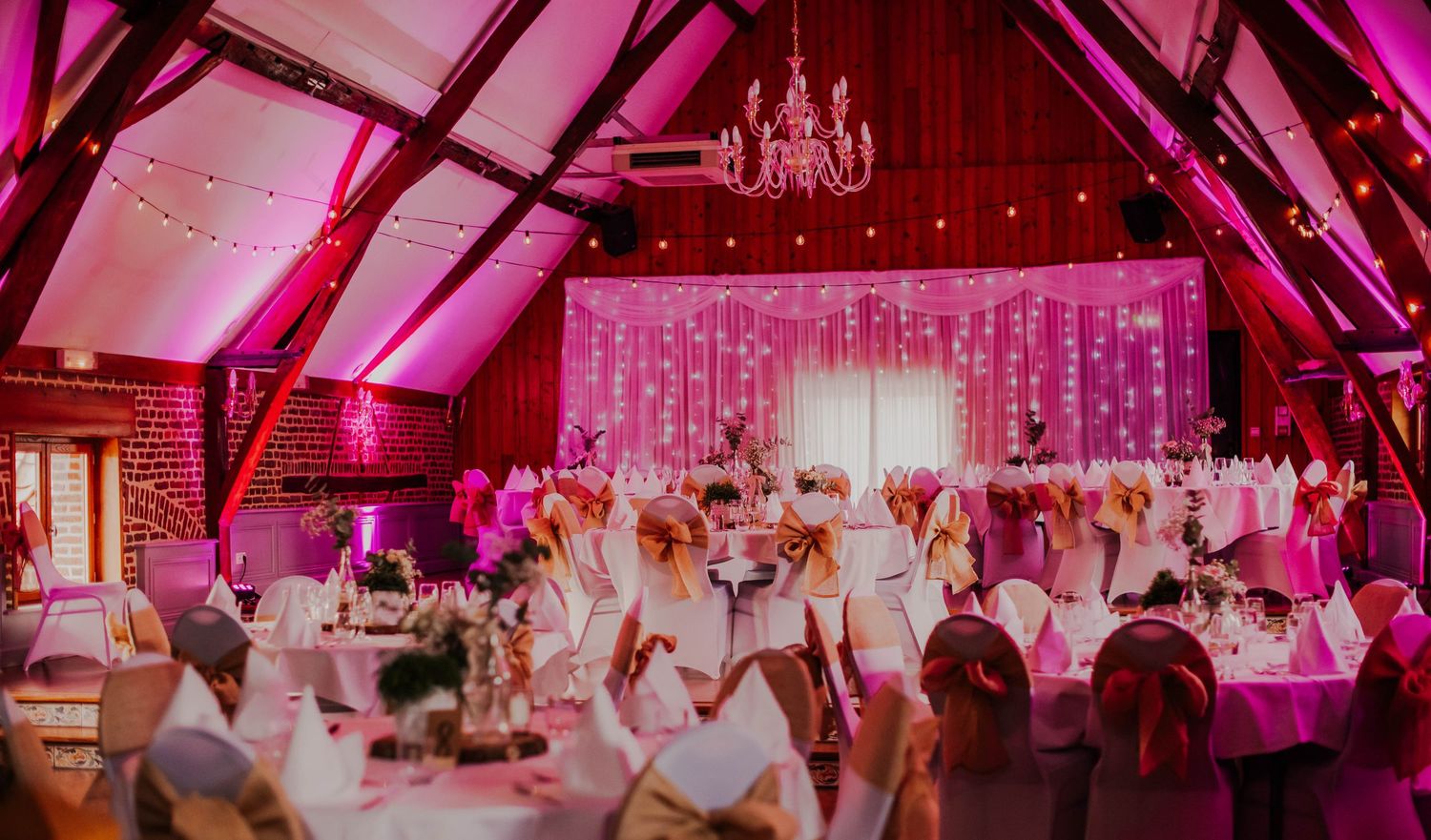 Wedding reception venue illuminated in vibrant pink lighting creating a romantic atmosphere.