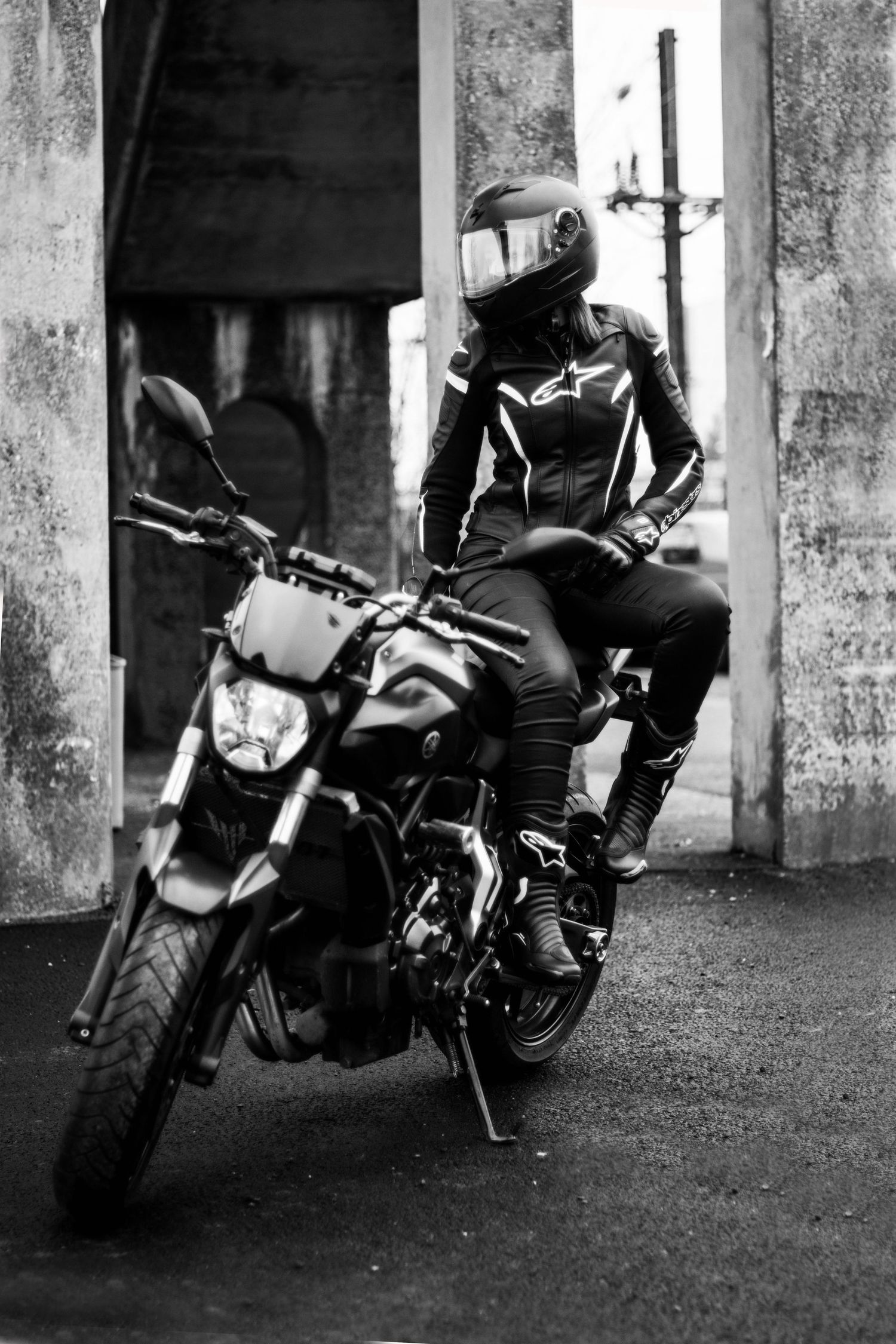 Motorcycle parked between concrete pillars in dramatic black and white composition.
