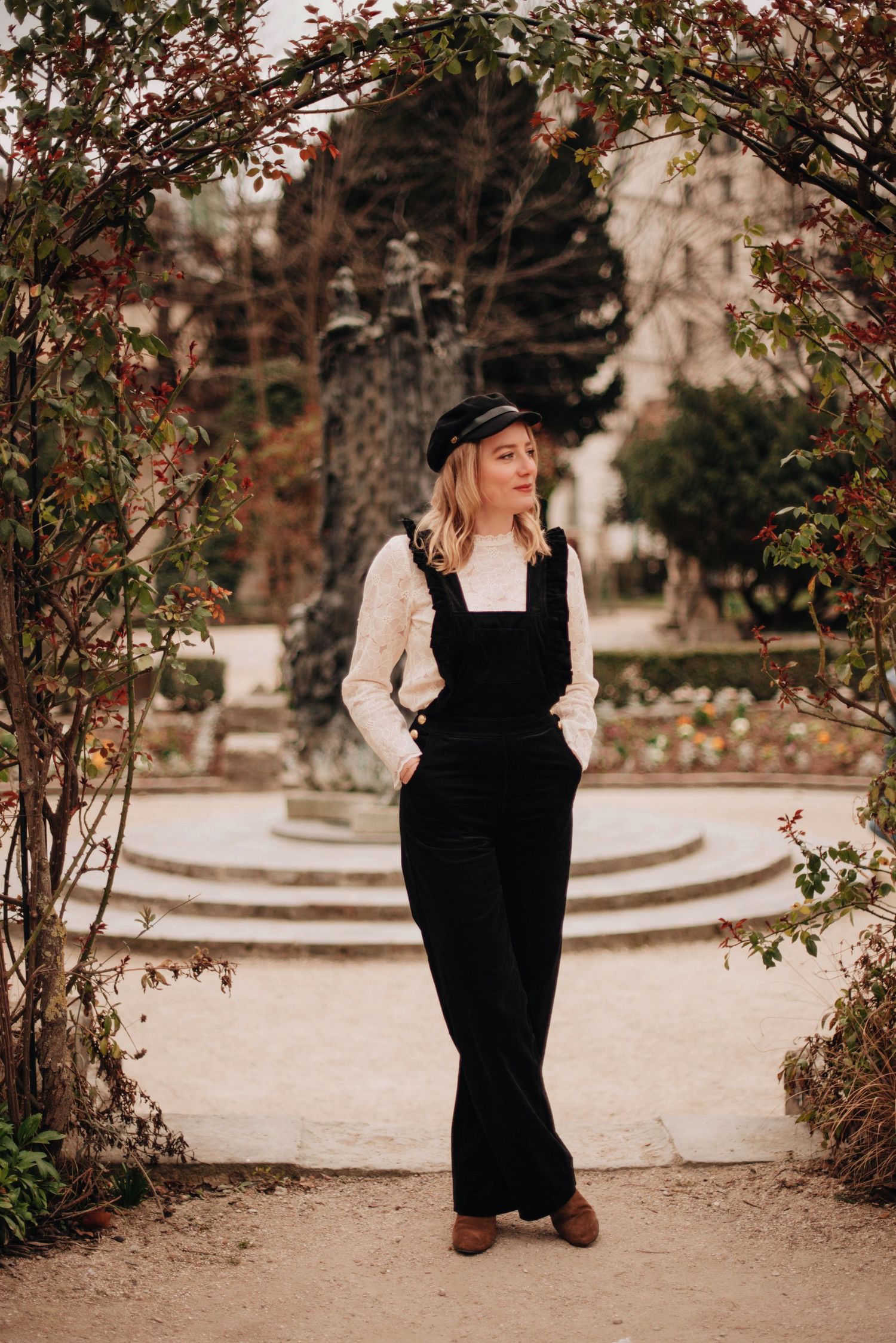 Person wearing black overalls and white blouse in an autumn garden setting.