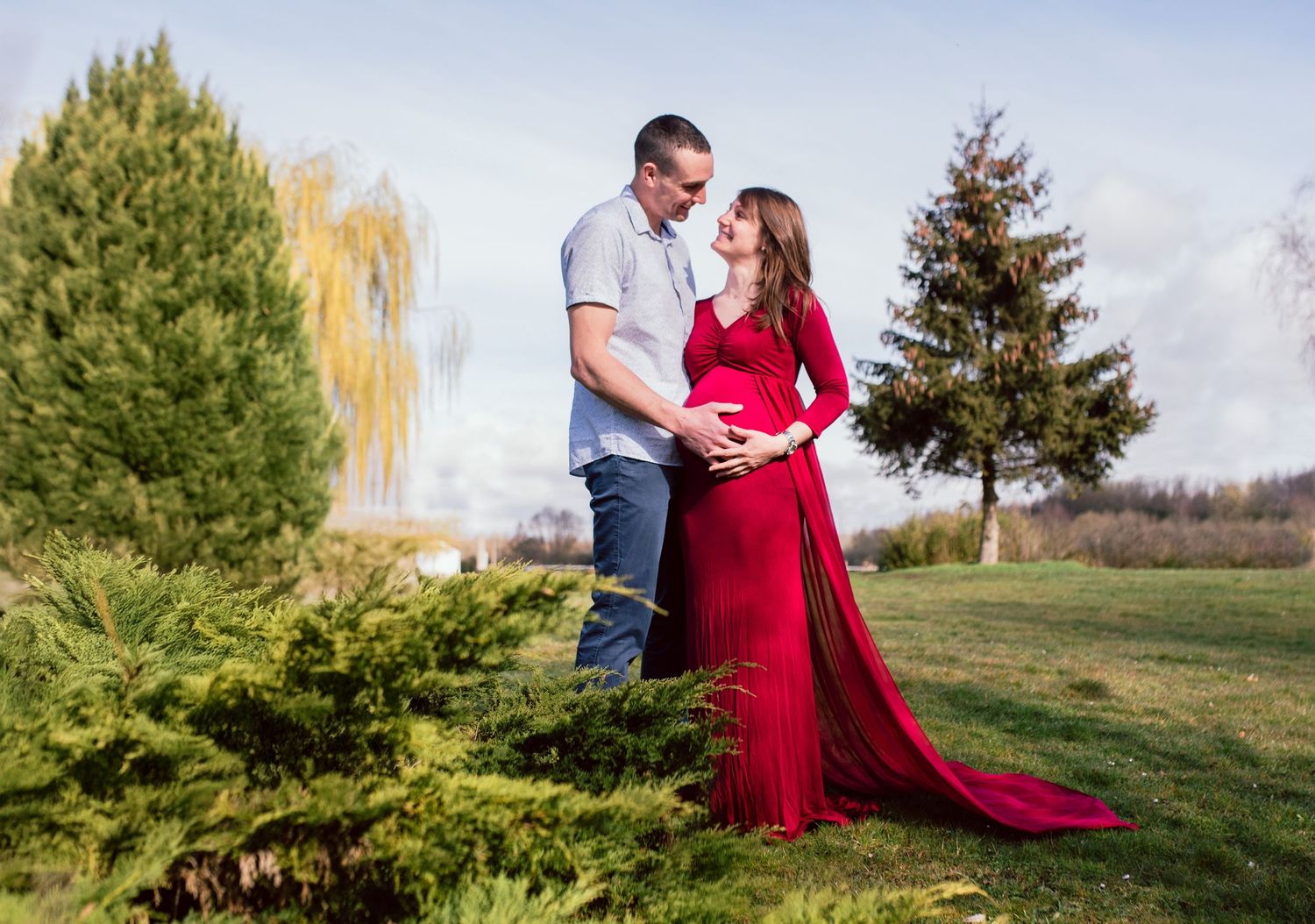 Scenic outdoor maternity photography session in a park with evergreen trees.