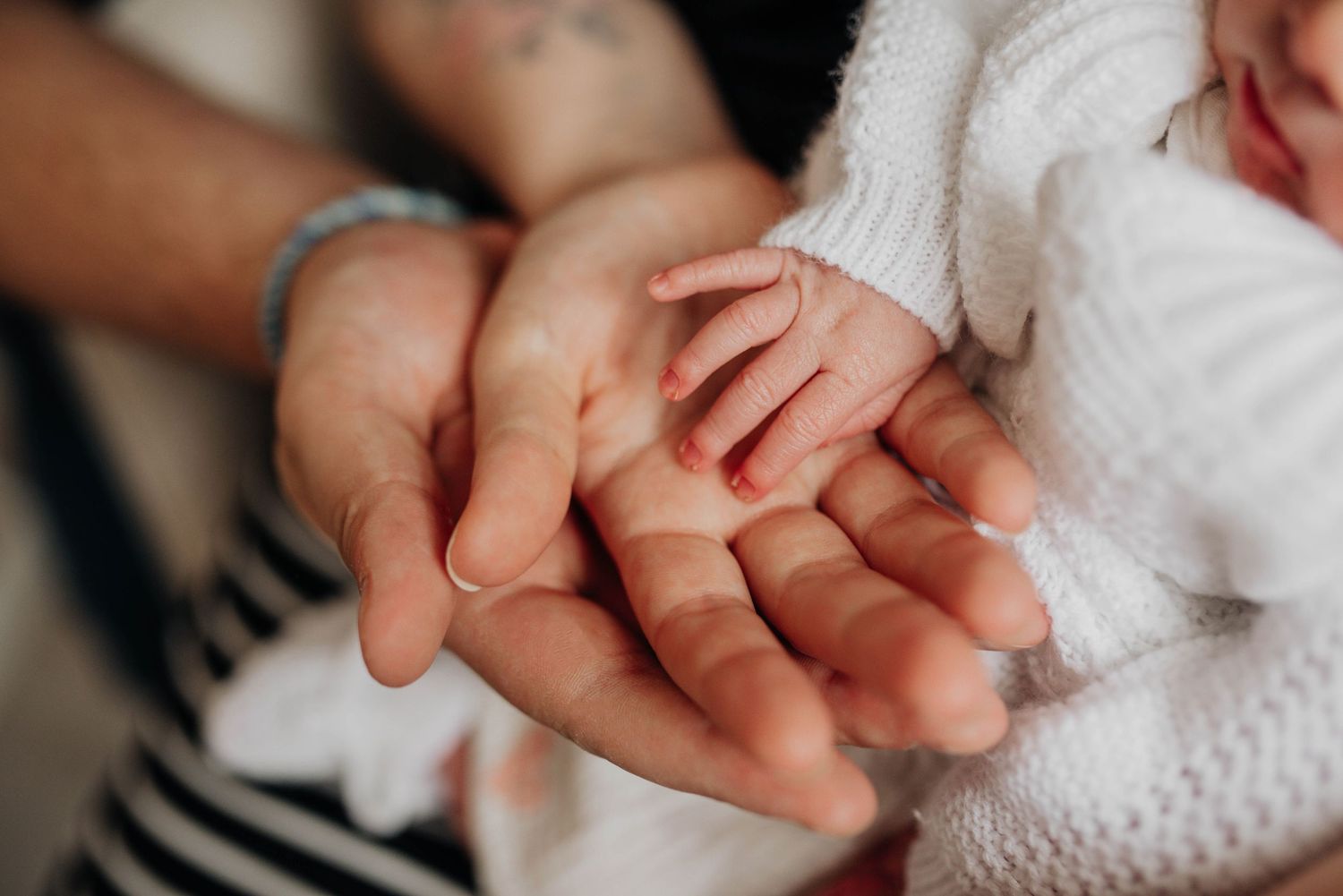 Close-up shot of tiny baby fingers grasping an adult hand in a gentle embrace.