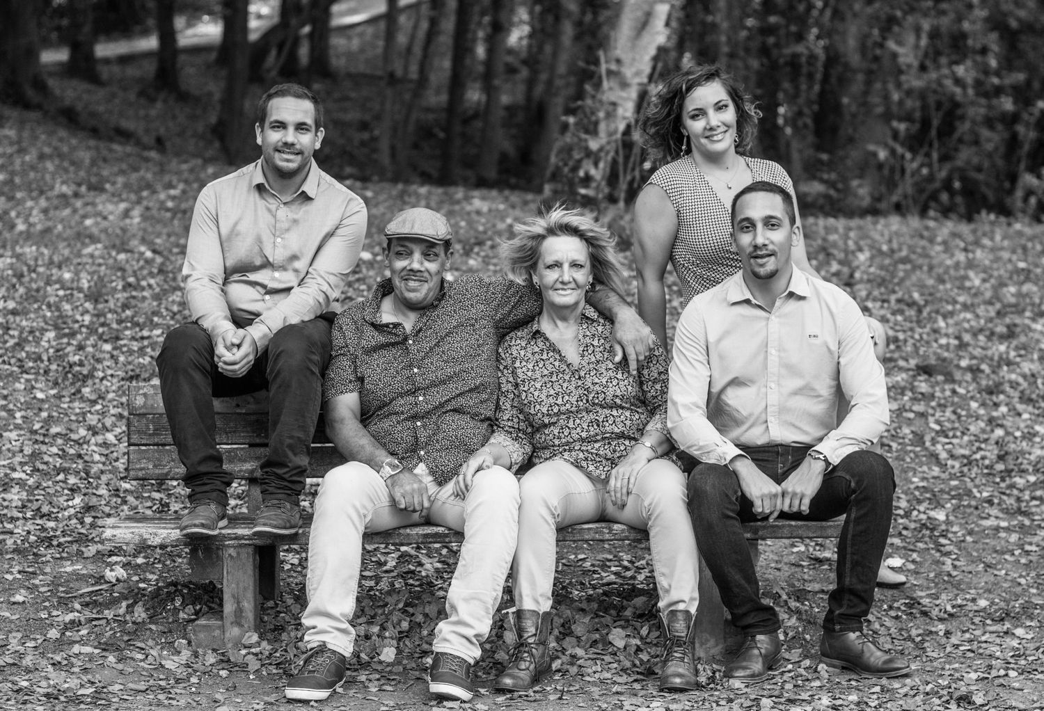 Family members sitting casually on fallen leaves in an autumn forest setting.