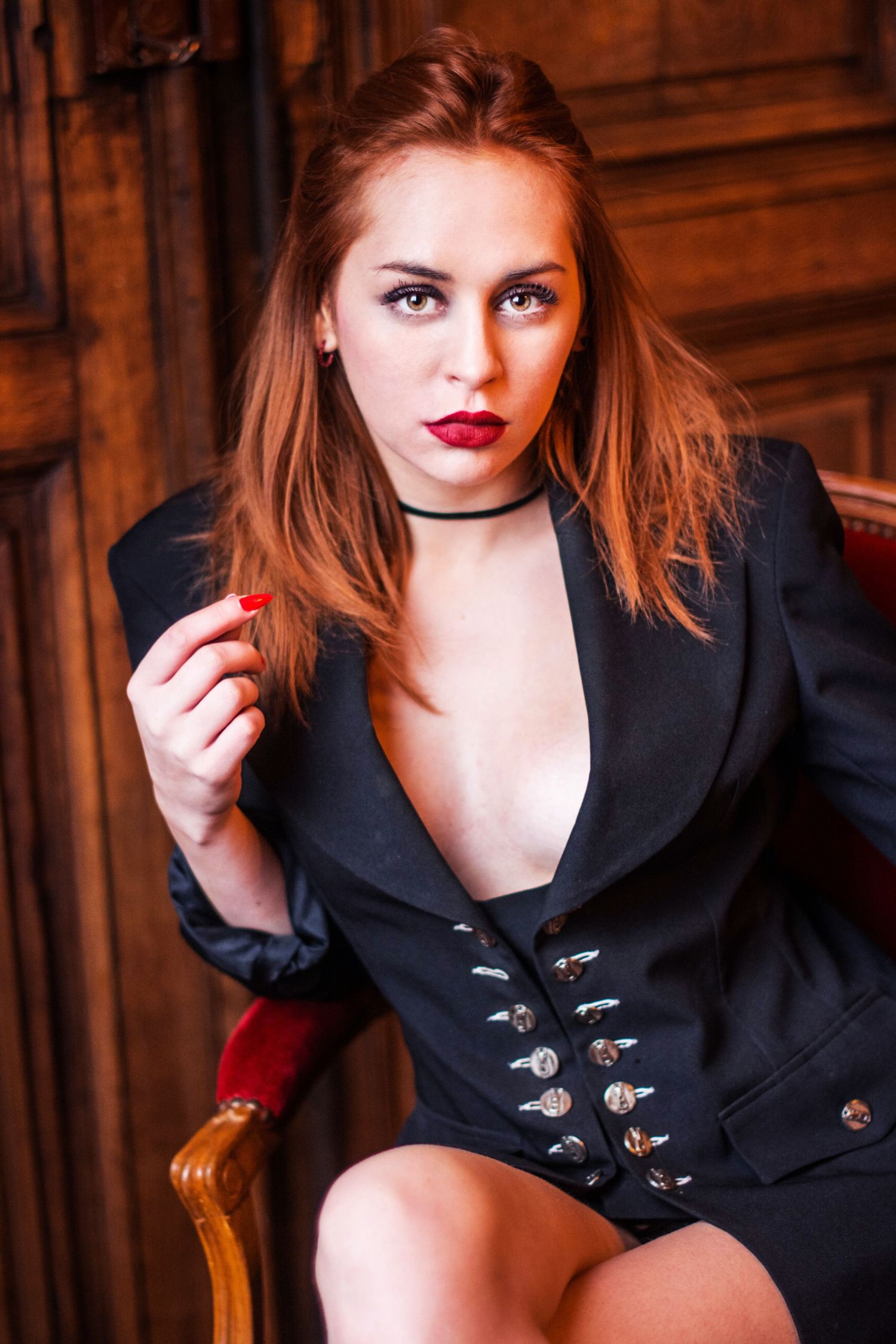 Fashion portrait of model in black blazer with decorative buttons against wooden backdrop.