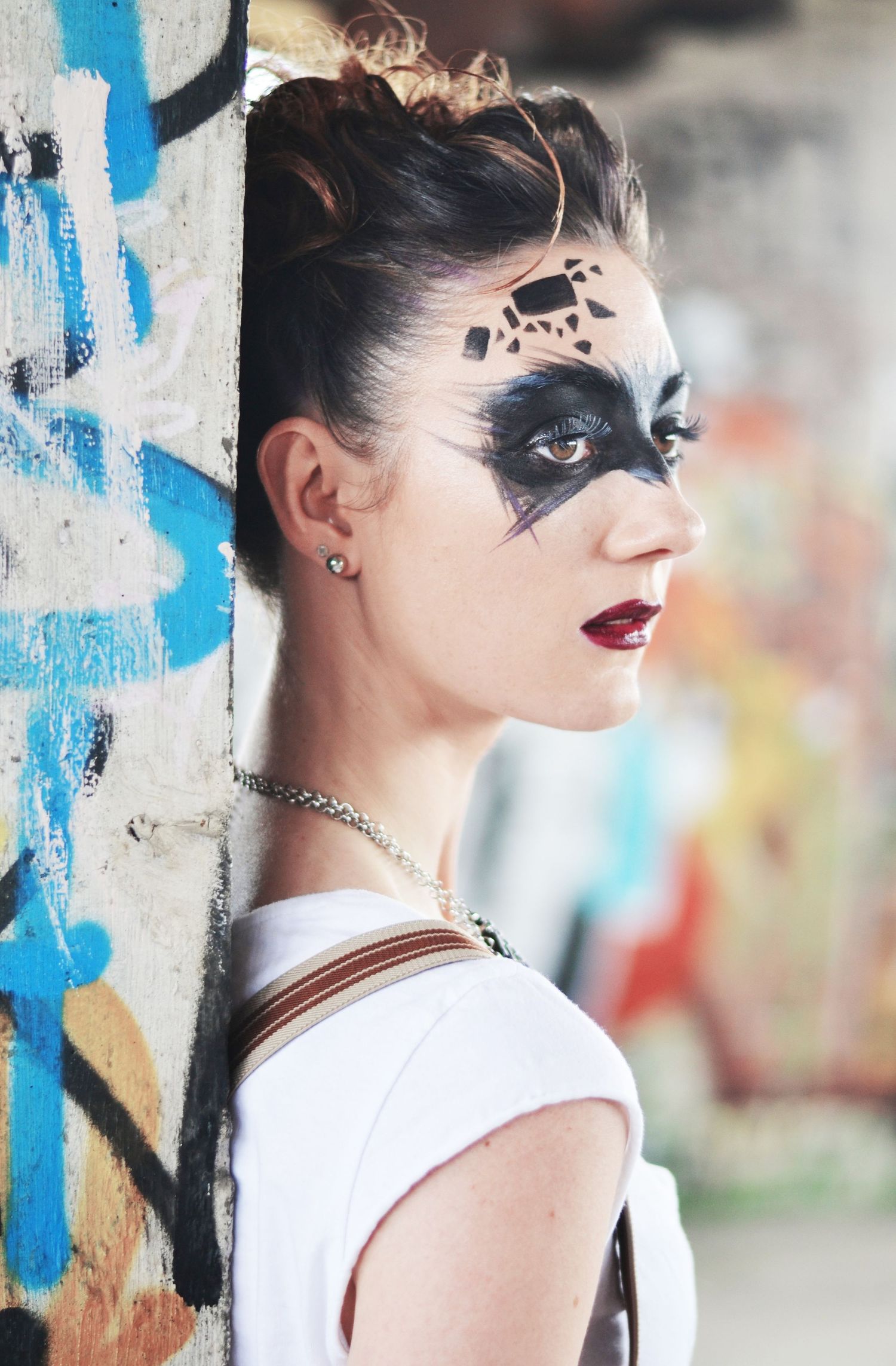 Edgy urban portrait with dramatic black face paint against graffiti wall.