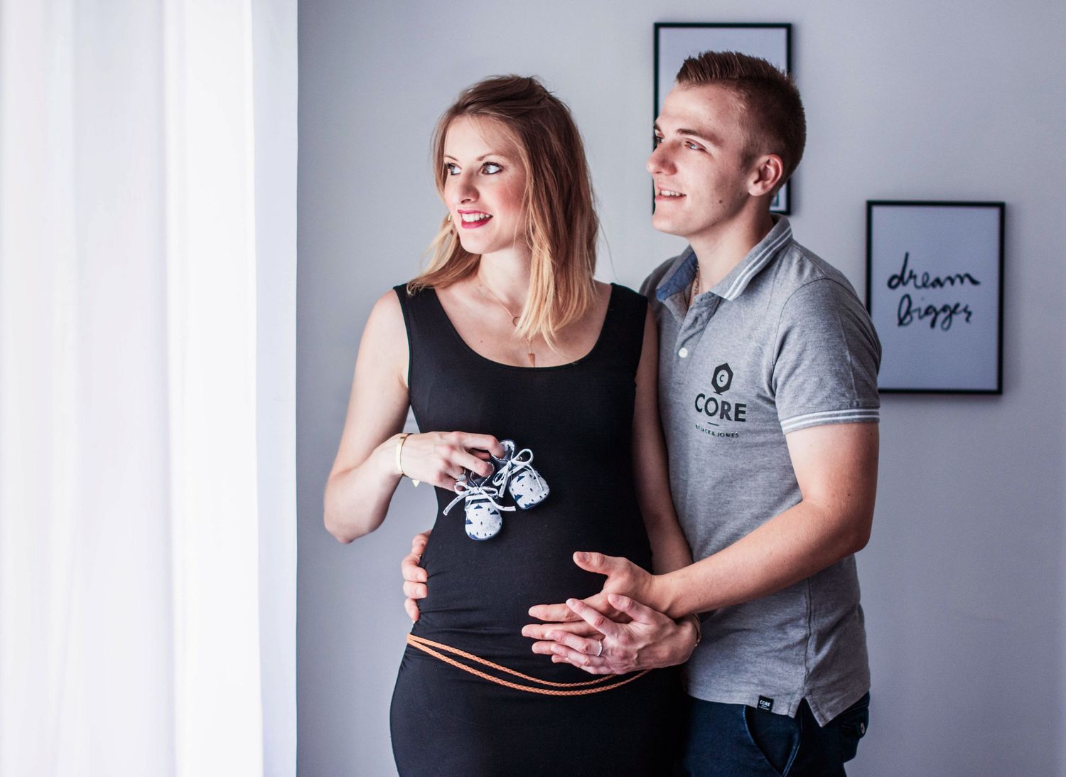 Maternity photoshoot with couple in casual attire against grey wall.