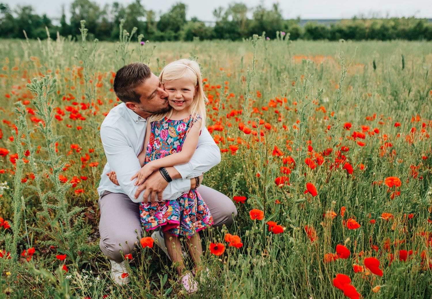 Family embracing in field of vibrant red poppies during golden hour.