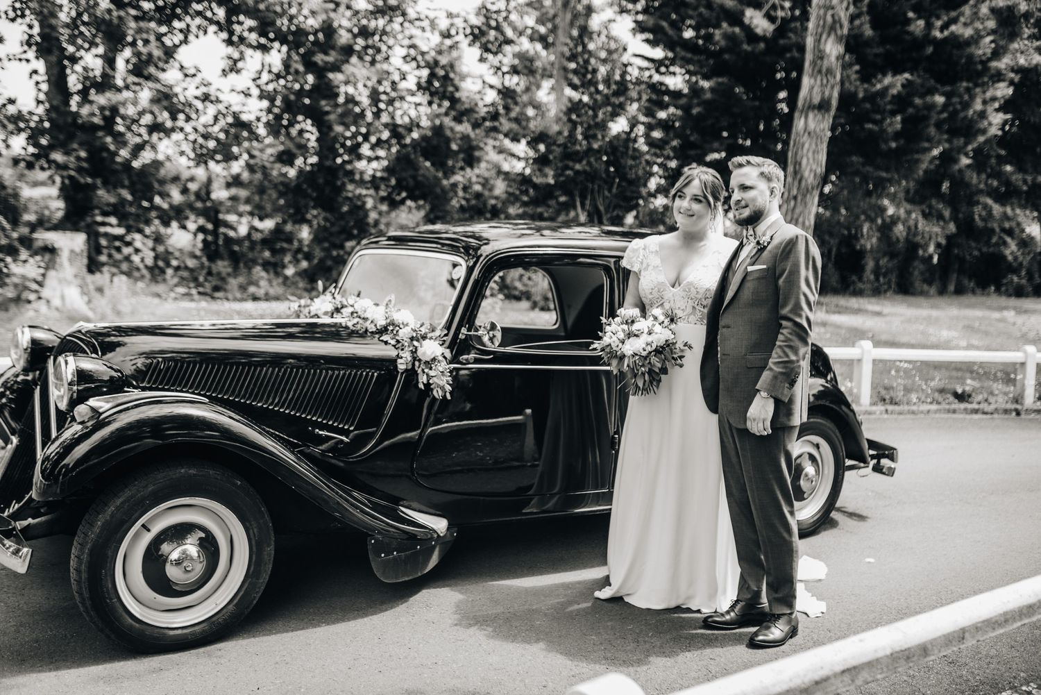 Classic vintage car parked outside with wedding party and guests gathered around it.