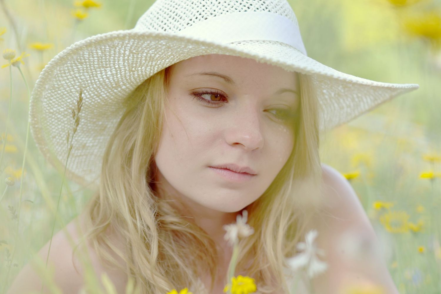Dreamy portrait in a field of yellow flowers wearing a white sun hat.