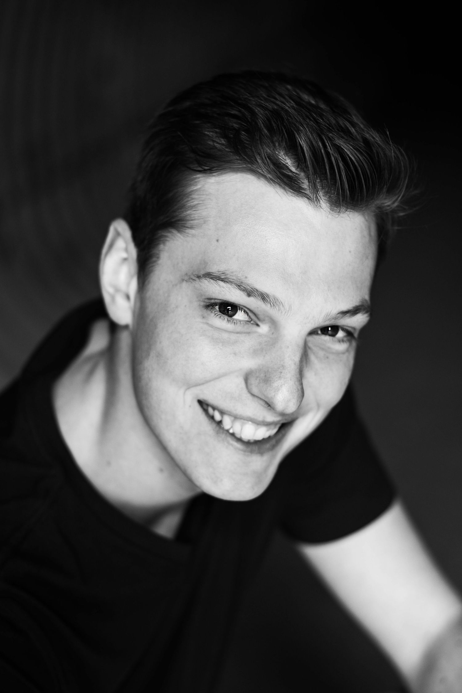 Black and white portrait of a smiling person in dark clothing against a dark background.