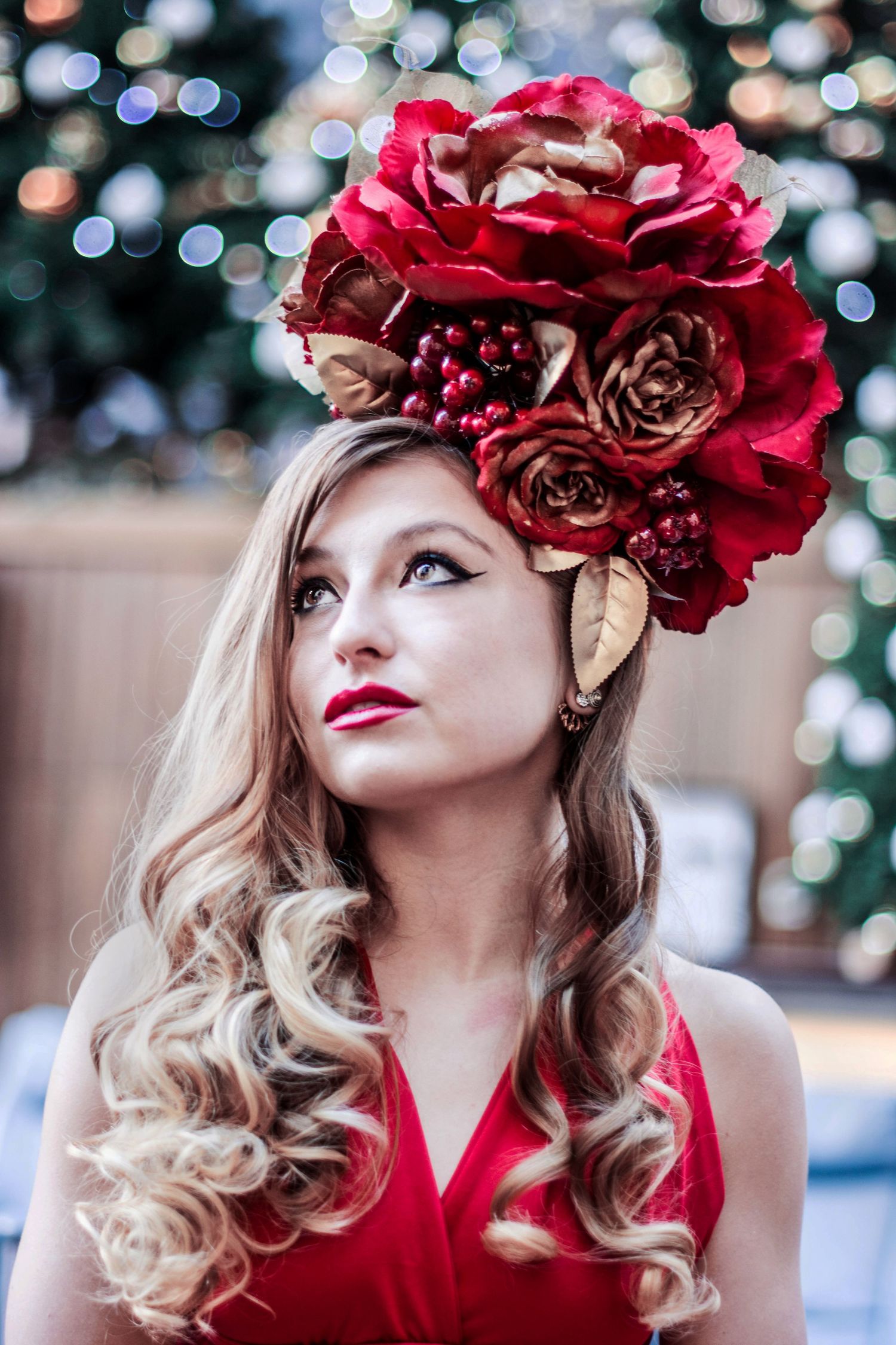 Elegant holiday portrait with red rose headpiece and curled hair against bokeh lights.