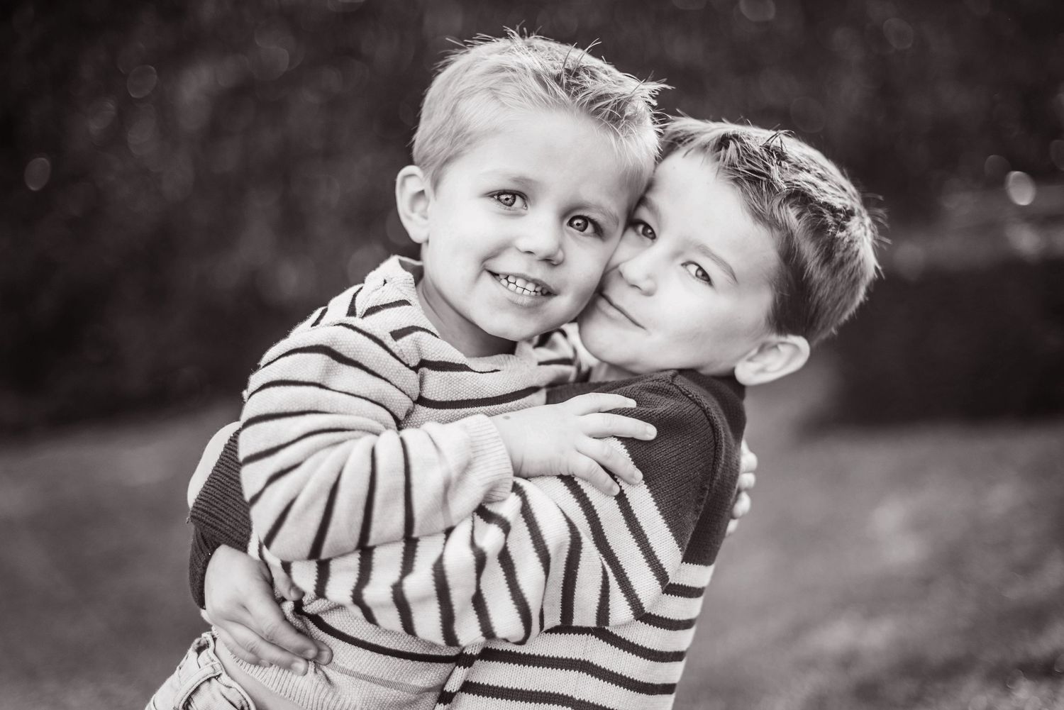 Two children in striped shirts sharing sweet moment in black and white portrait.