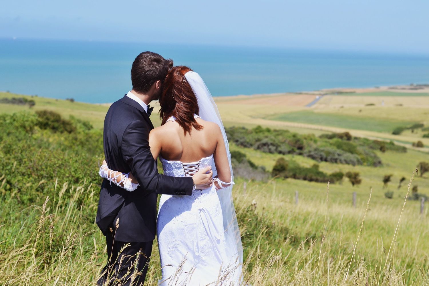 Wedding couple stands together against scenic coastal landscape with rolling hills.