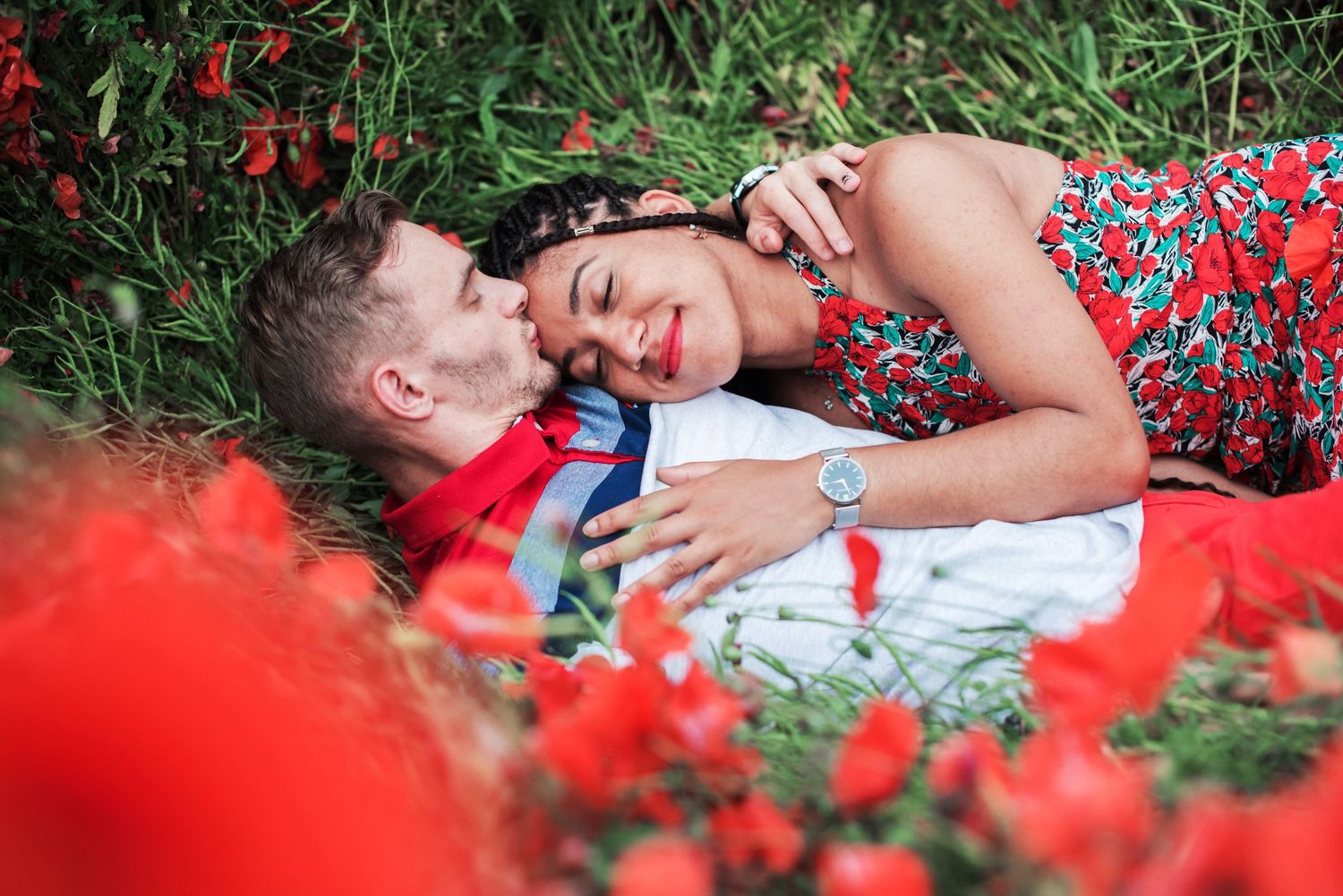 Romantic couple lying together in field of red poppies.