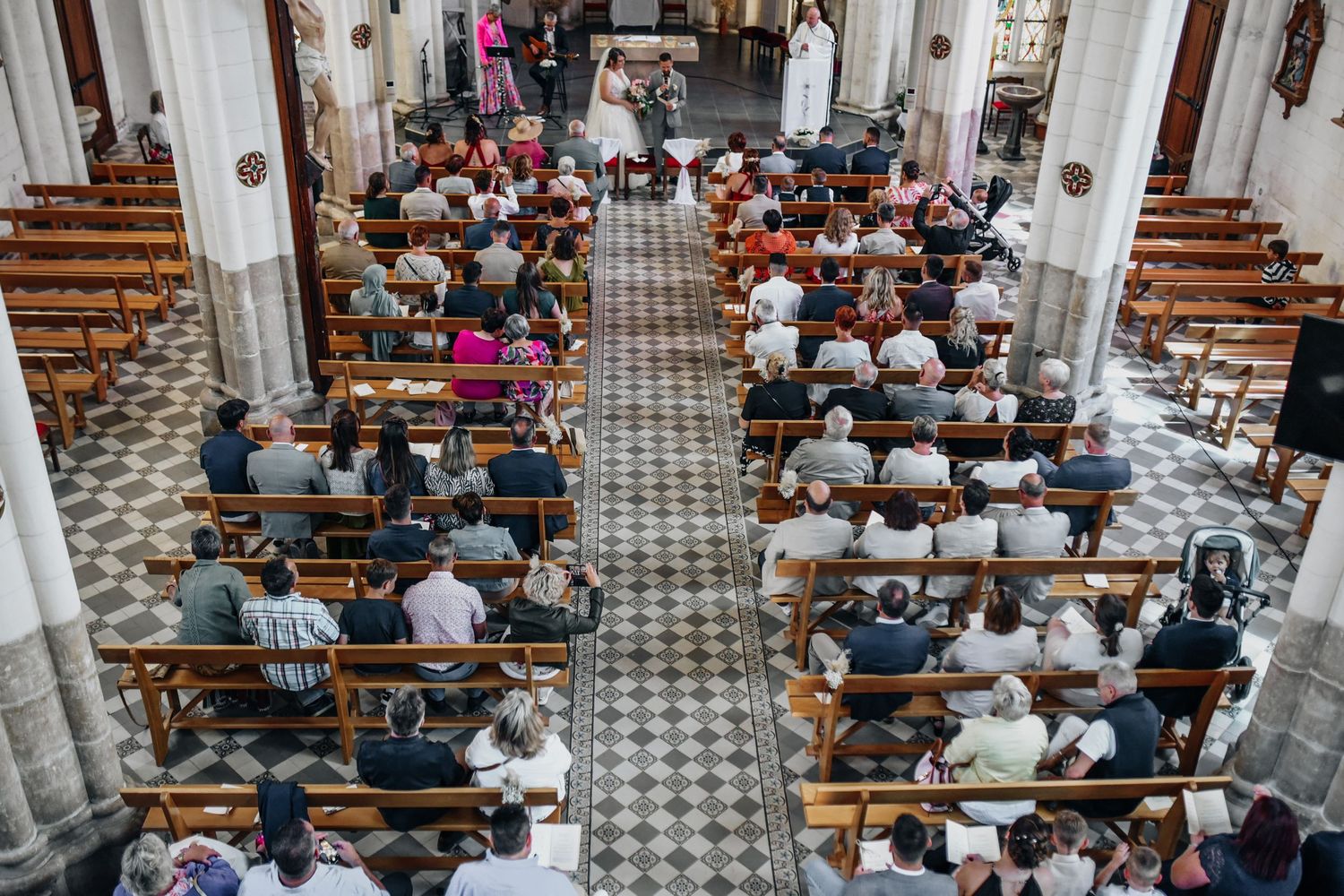 Wide angle view of church interior during wedding ceremony with guests seated in pews.