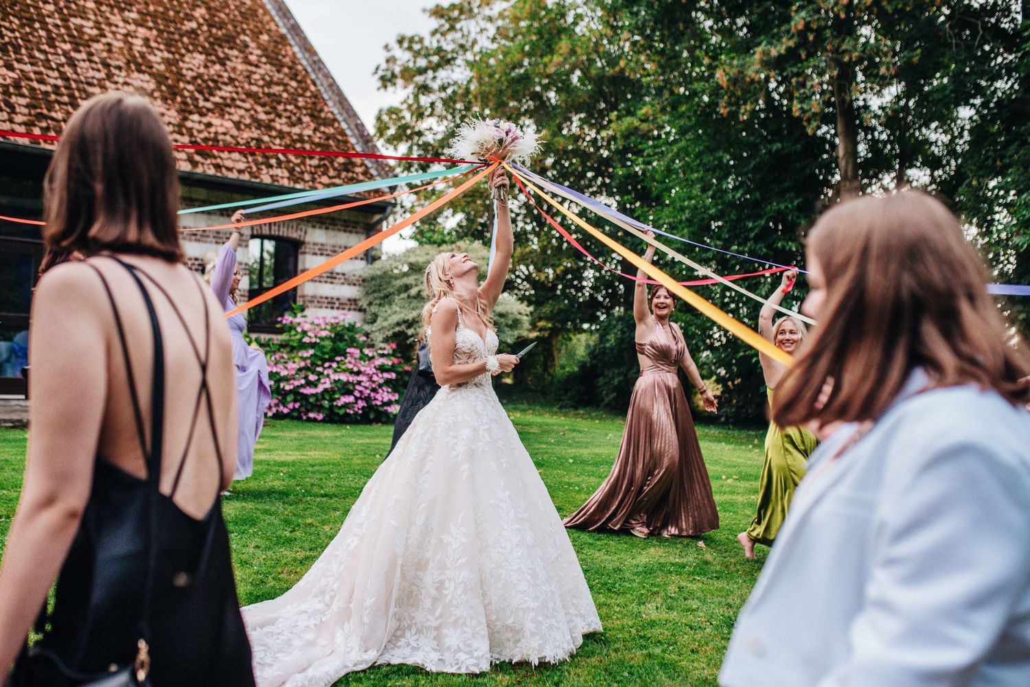 Wedding party celebrates outdoors with streamers and a beautiful white lace gown against a rustic barn backdrop.