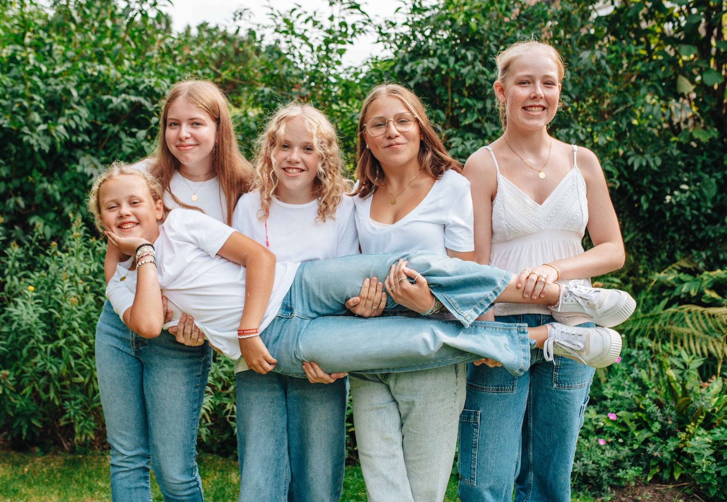 A playful group portrait of people in matching outfits holding each other in a garden setting.