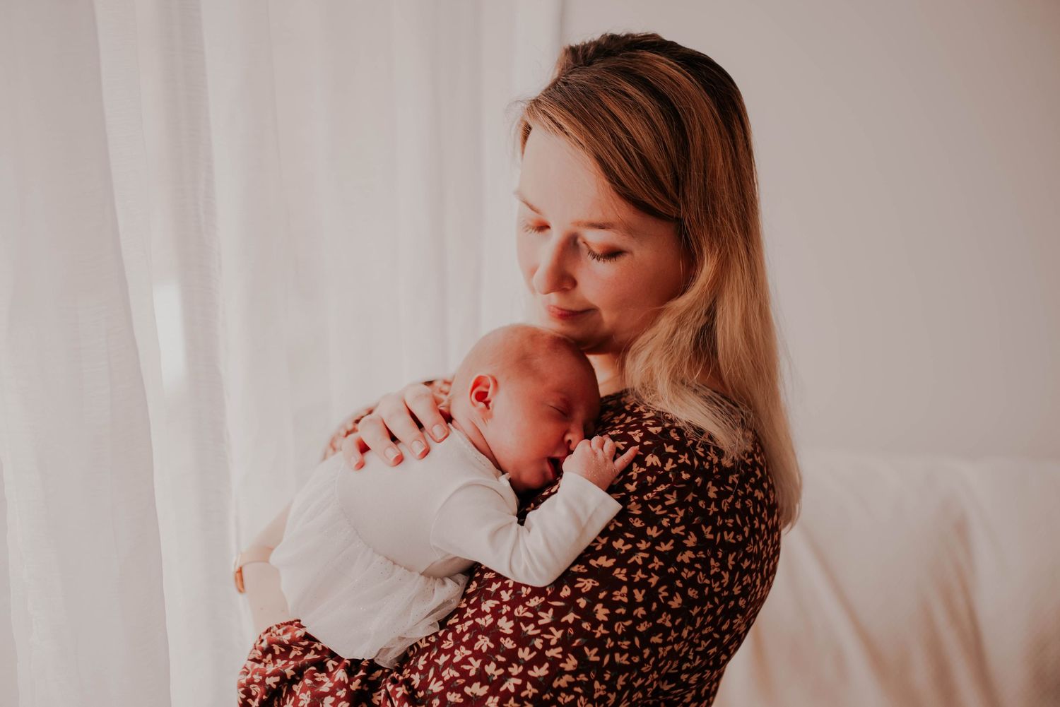 Newborn baby sleeps peacefully in soft pink blanket while being cradled.