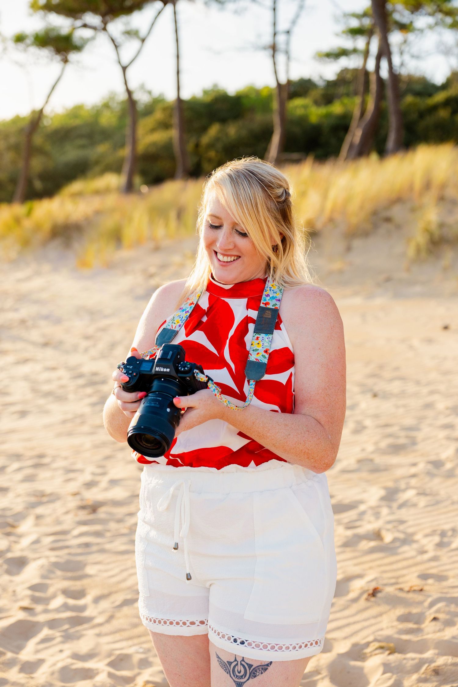 Photographer poses with camera gear on sandy beach during golden hour.
