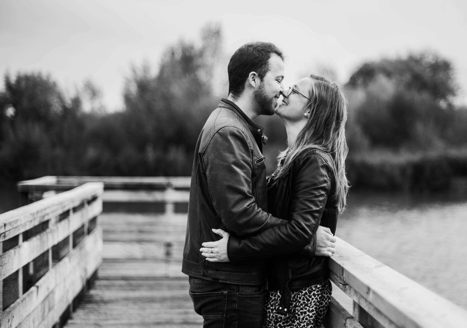 A romantic couple embraces on a wooden bridge in black and white photography.