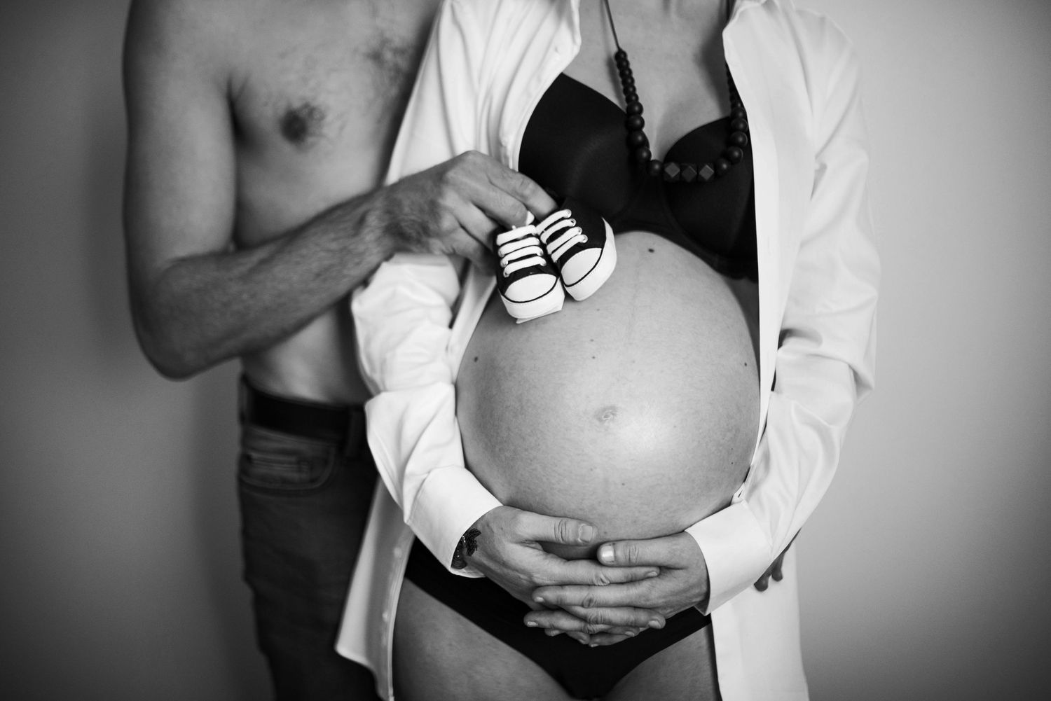 Black and white maternity photo with tiny baby shoes held against pregnant belly.