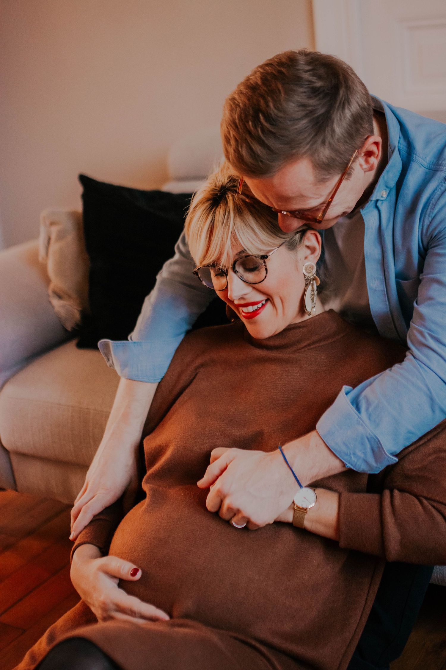 Intimate moment between expectant couple on couch as they lovingly embrace and touch pregnant belly.