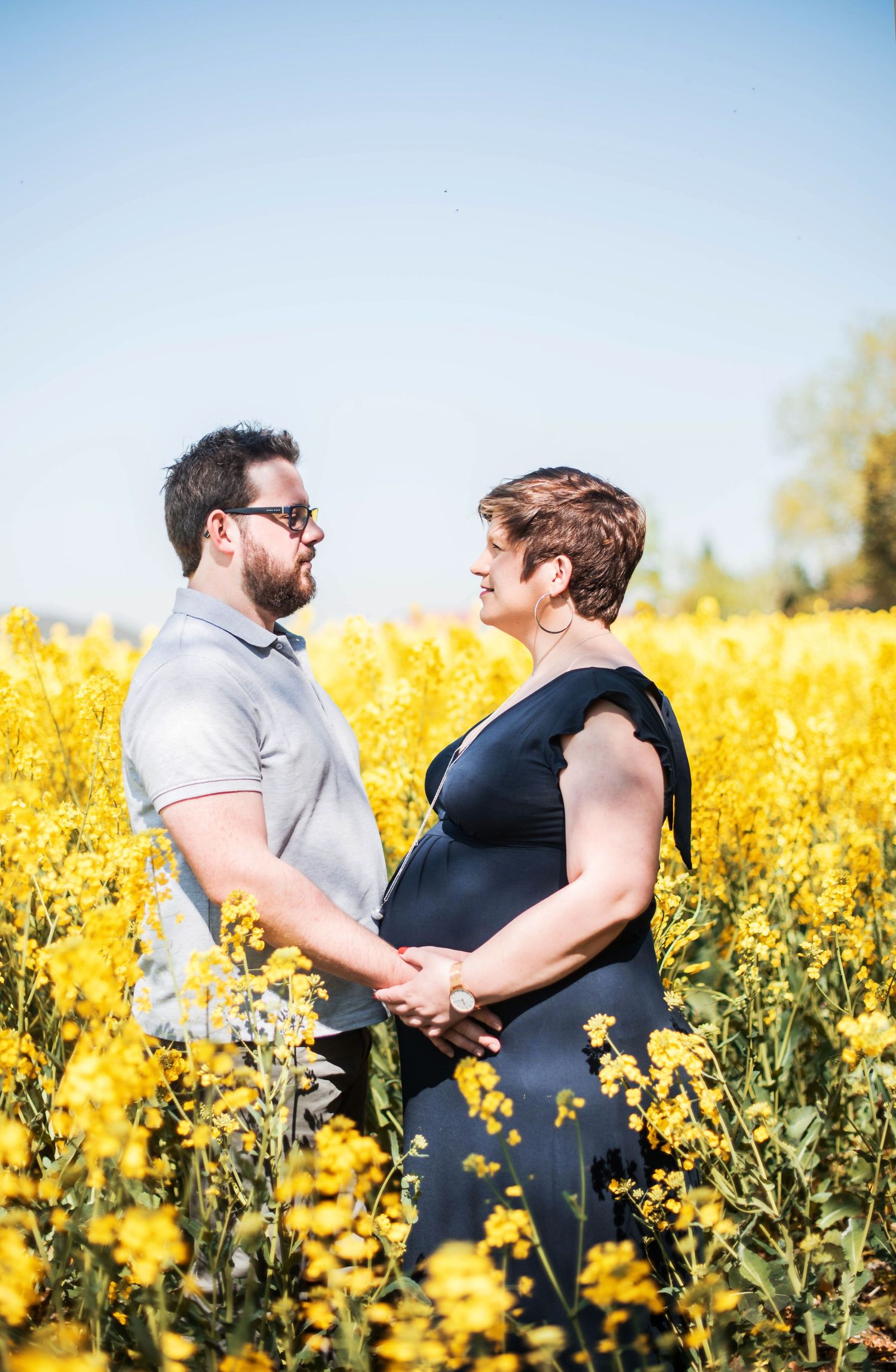 Couple posing together in blooming yellow canola field on sunny day.