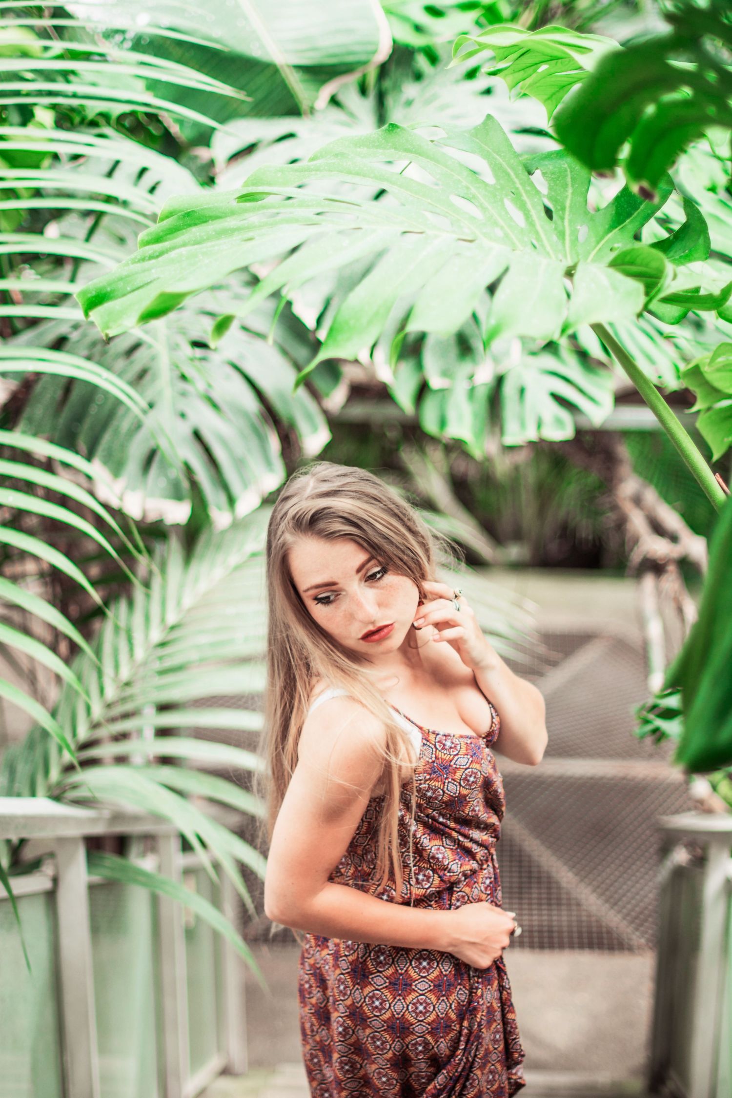 Tropical greenhouse portrait with large monstera leaves framing a patterned summer dress.