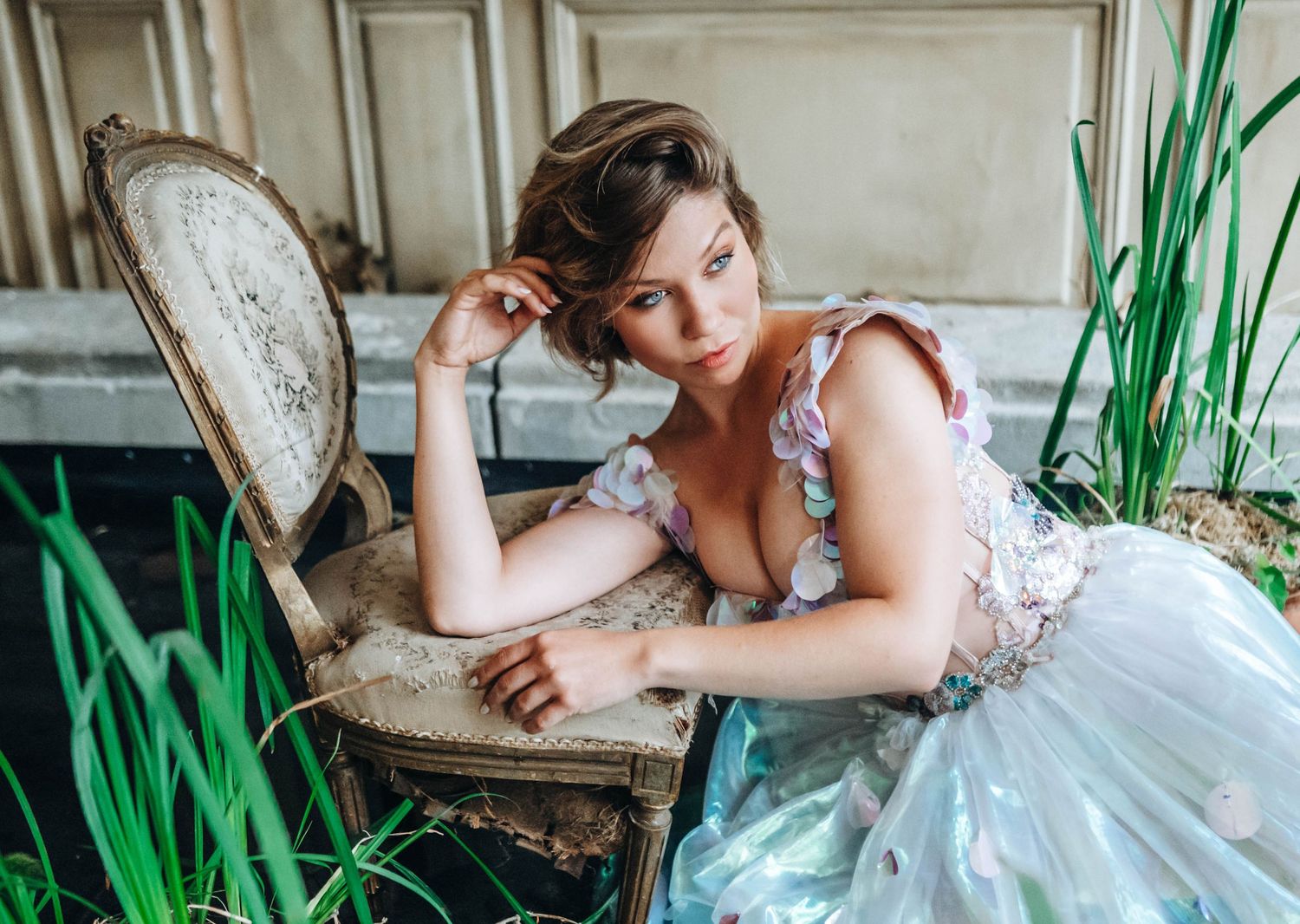 Ethereal photoshoot featuring a white lace dress against vintage furniture and green plants.
