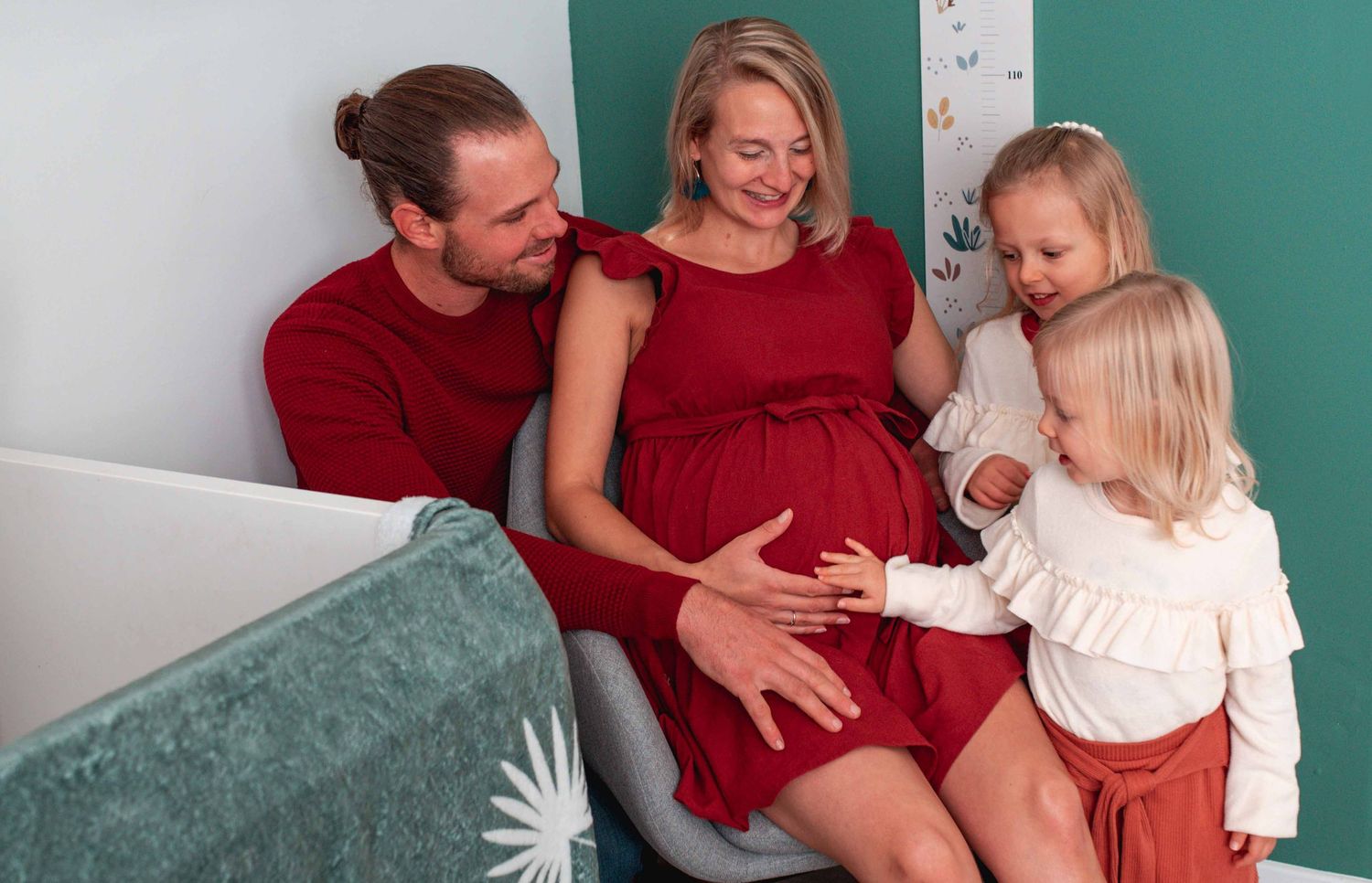 Family maternity session against teal wall with coordinating red and white outfits.