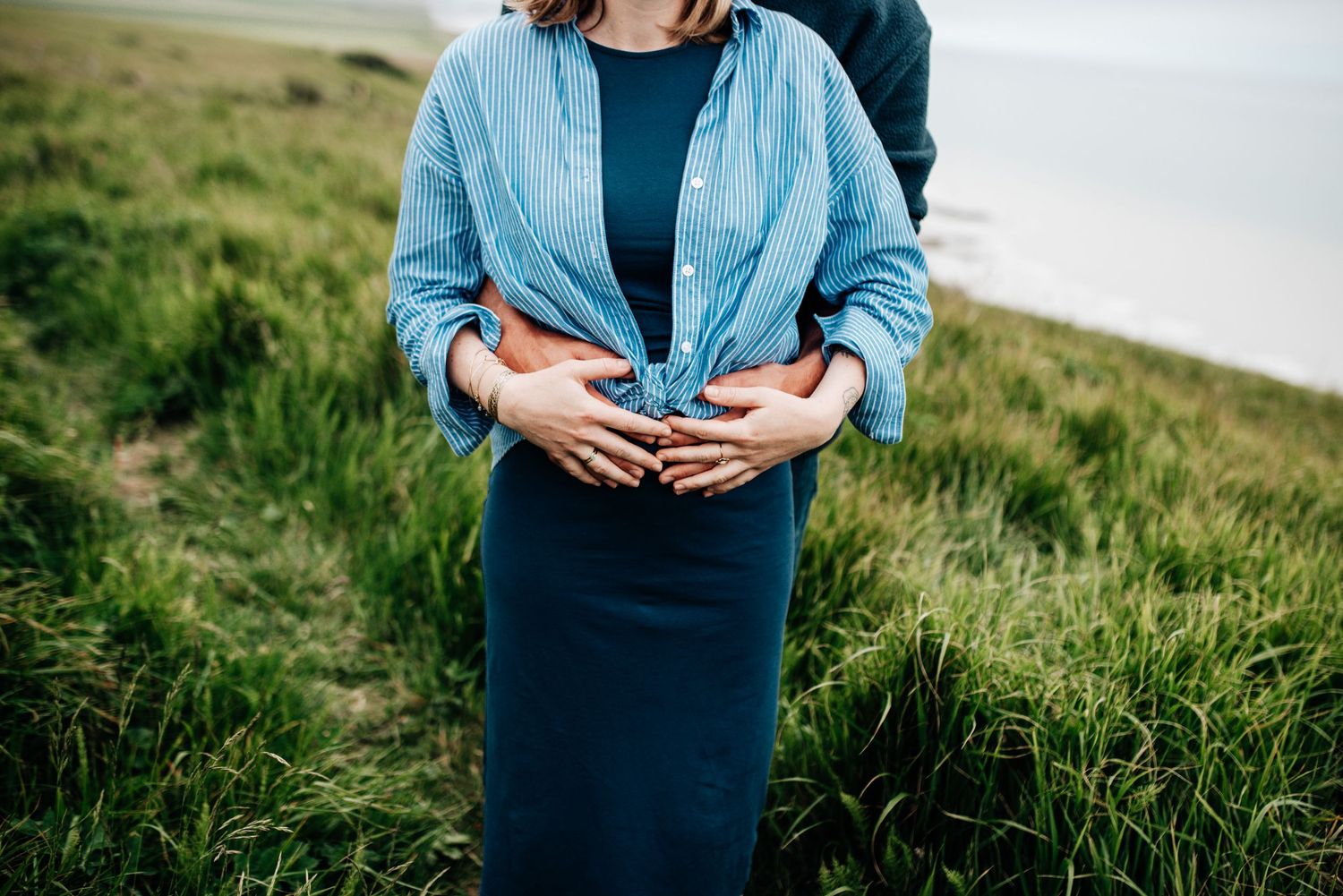 Couple embracing in a grassy meadow wearing coordinating blue and navy outfits.