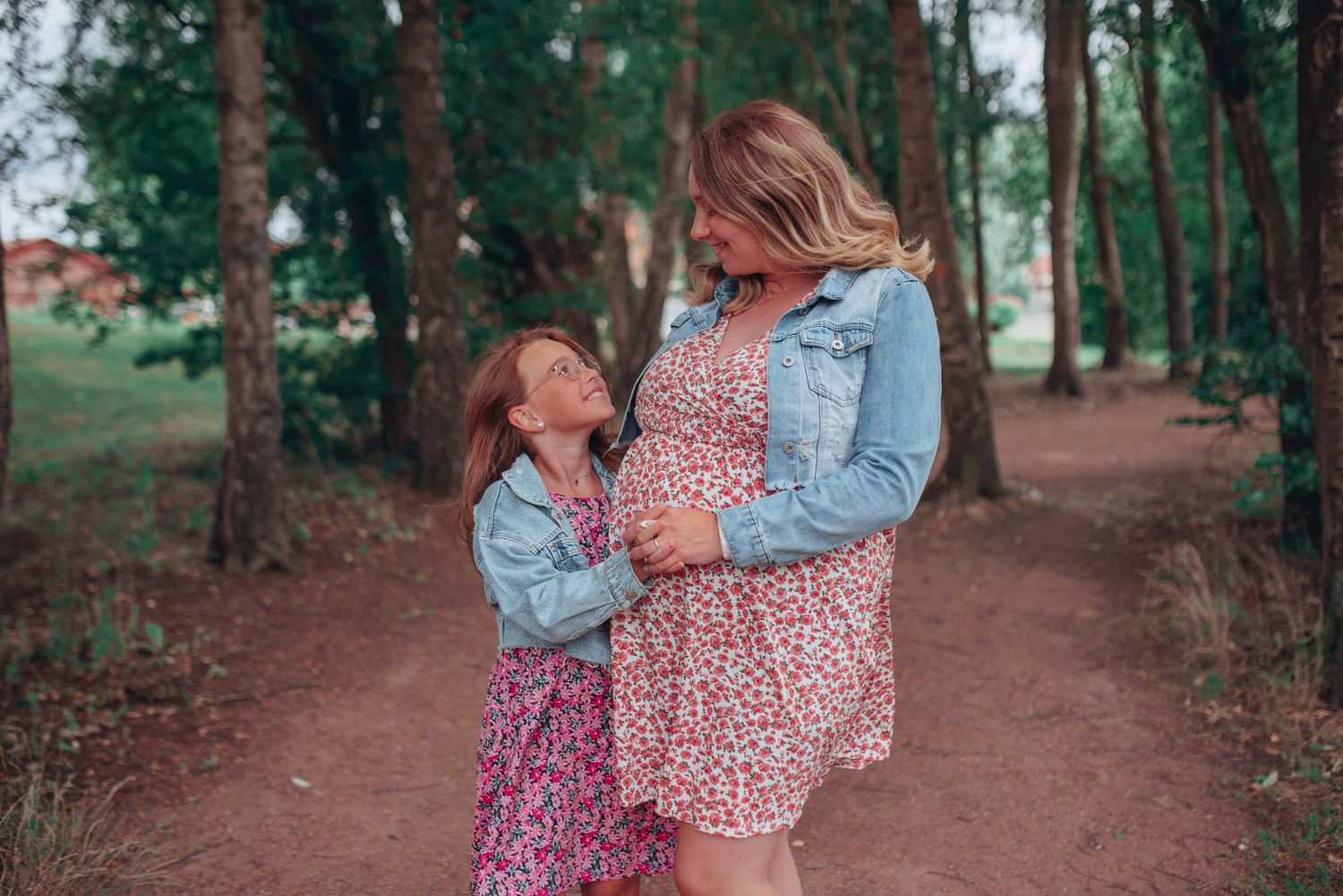Couple walking together on a tree-lined path during a maternity photoshoot.