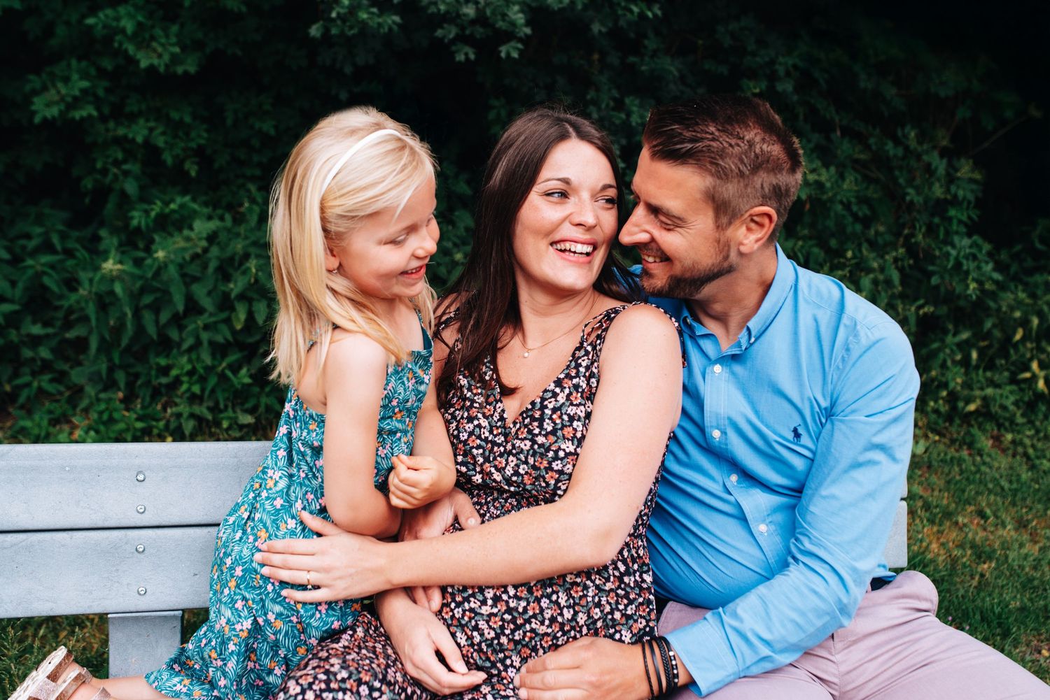 Intimate family moment captured on white bench in outdoor garden setting.
