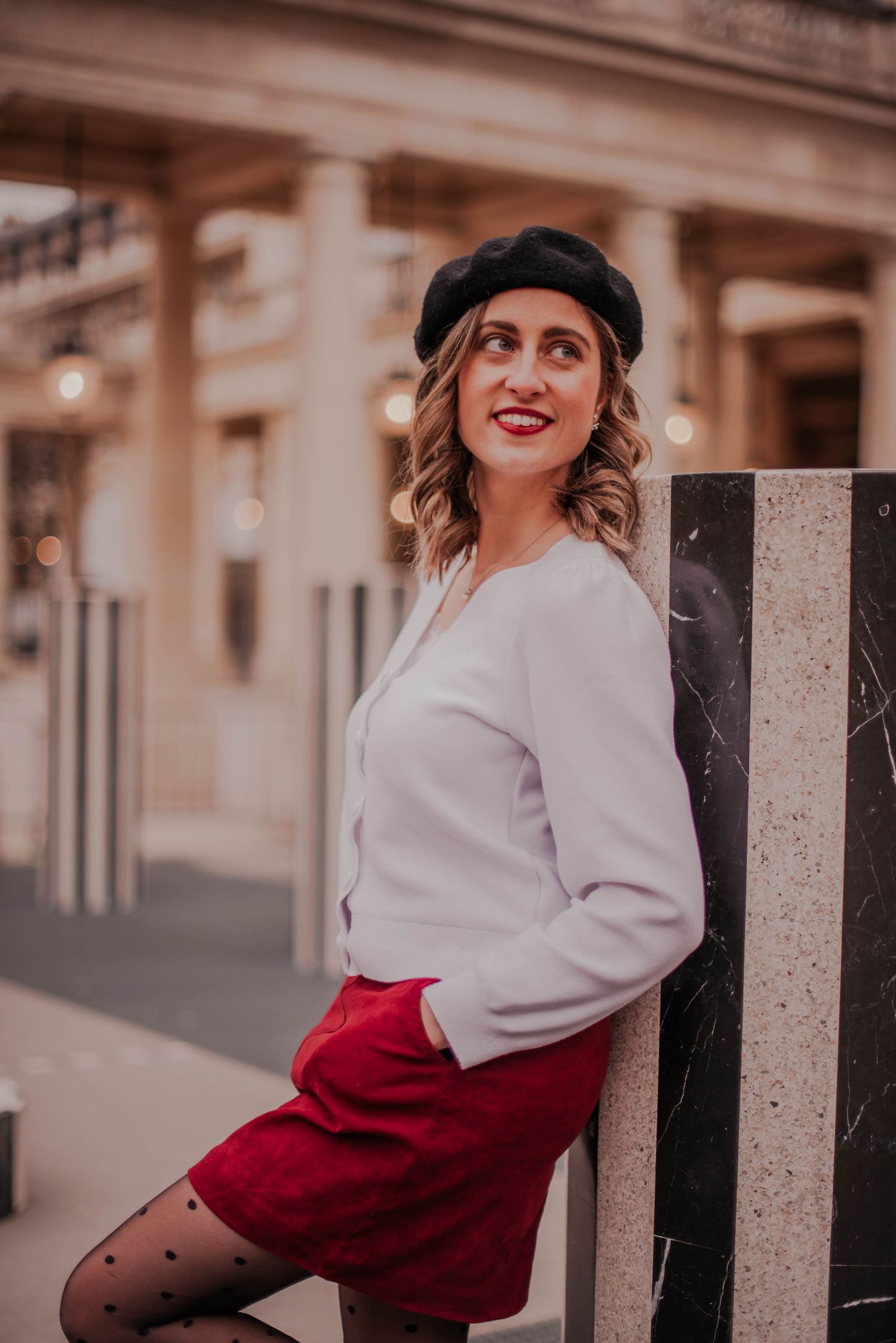 Vintage-inspired outfit with red skirt and white sweater against urban backdrop.