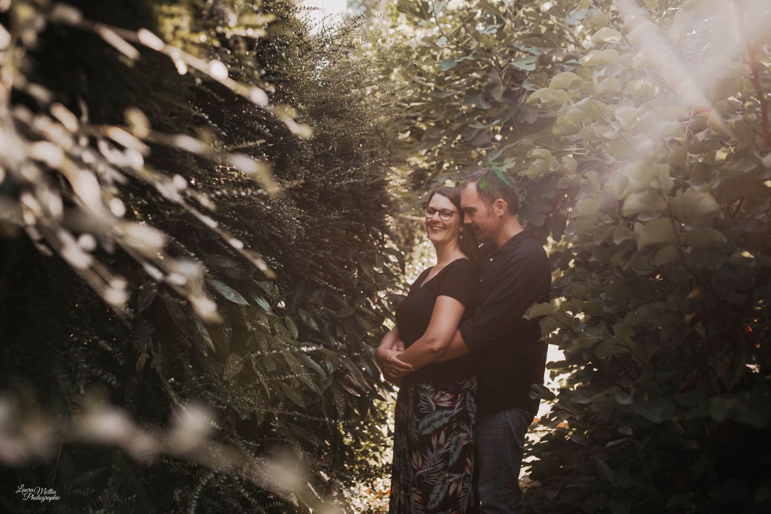 Silhouetted couple embracing in dreamy sunlit forest setting.