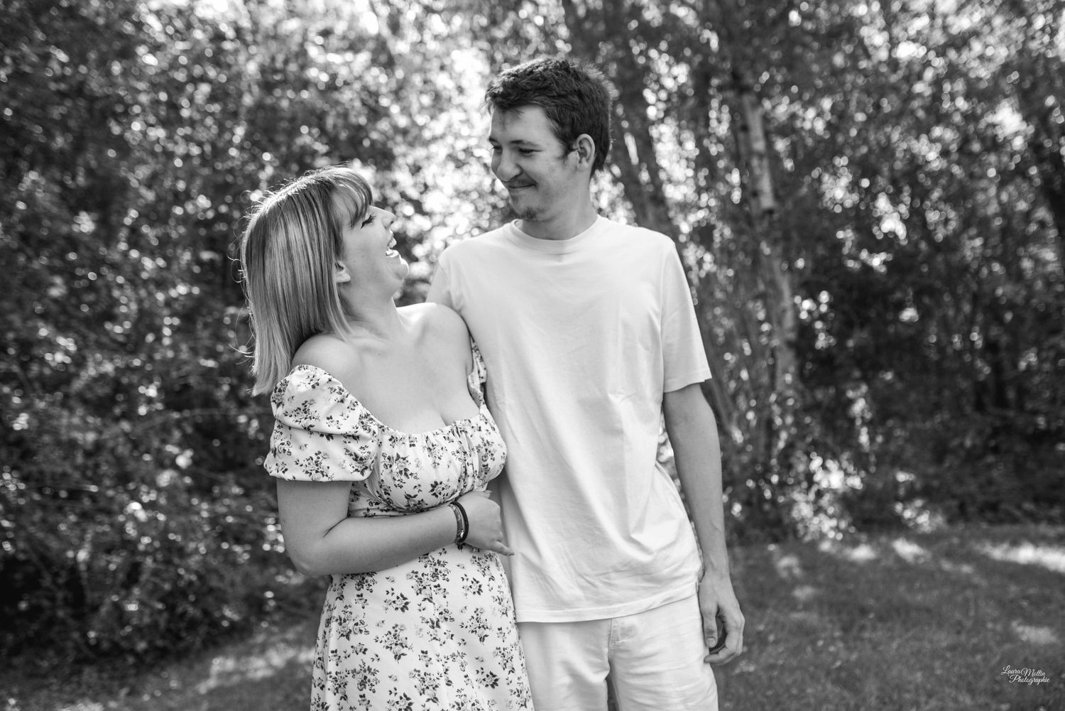 Black and white photo of couple laughing together in casual summer outfits against garden backdrop.