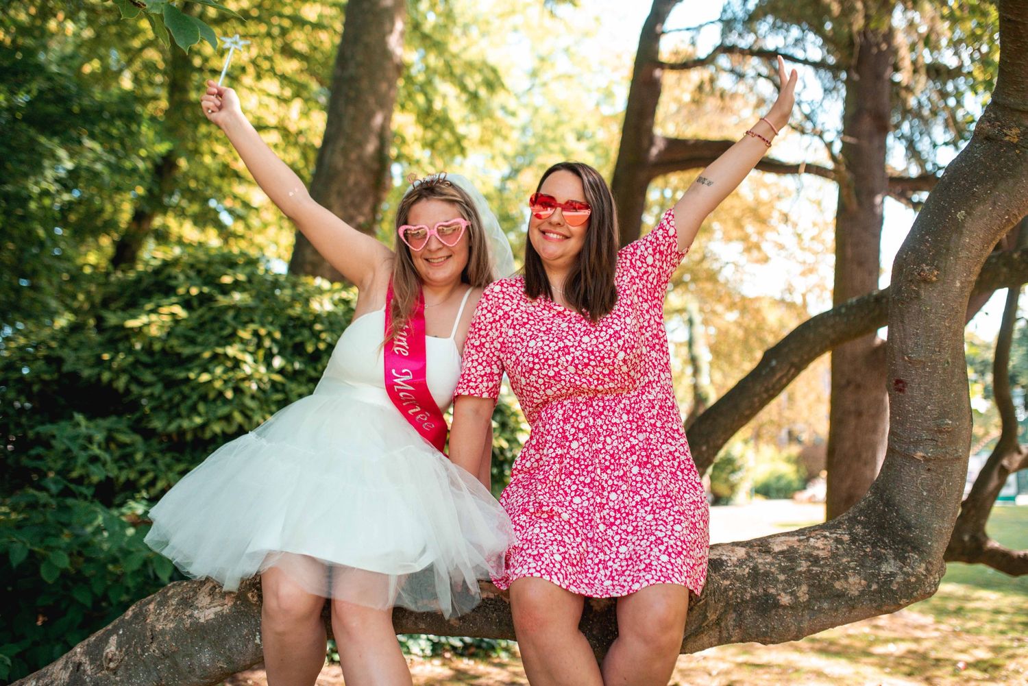 Two friends pose playfully on a stone wall in pink and white outfits.