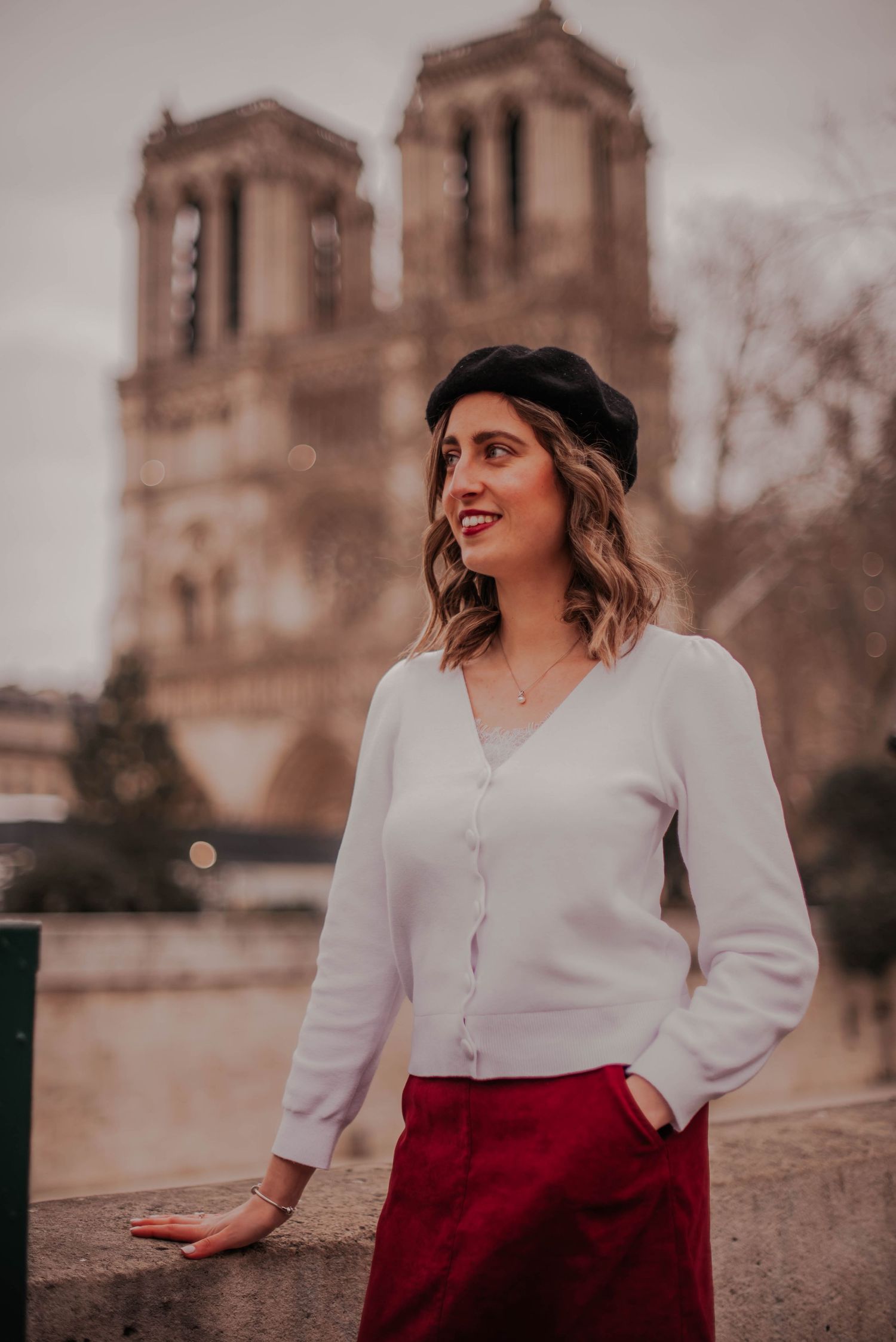 Woman in white blouse and red skirt posing near Notre Dame Cathedral in Paris.