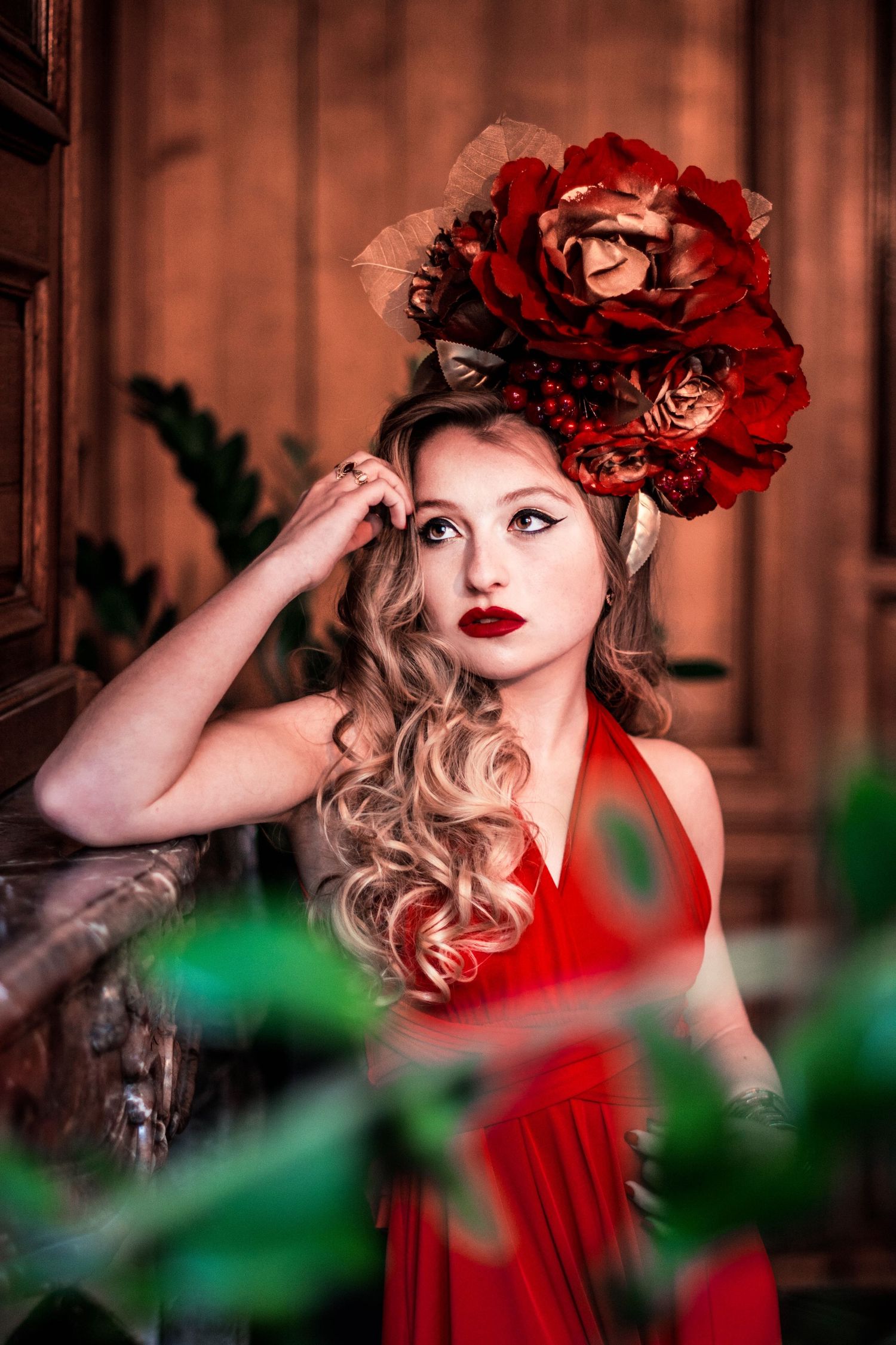Portrait featuring red roses headpiece and matching red dress against wooden backdrop.