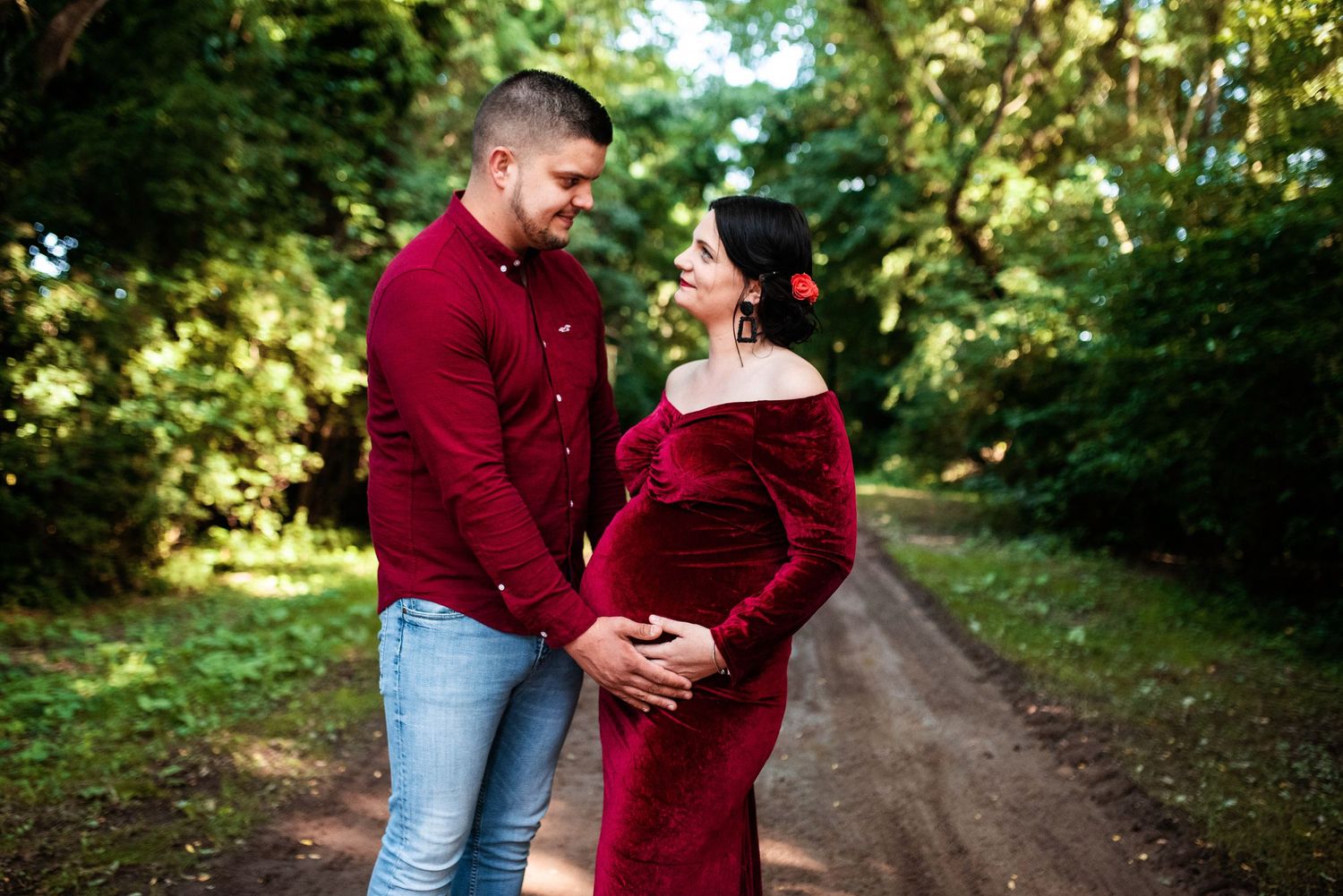 Couple shares intimate moments on a forest path wearing burgundy outfits.