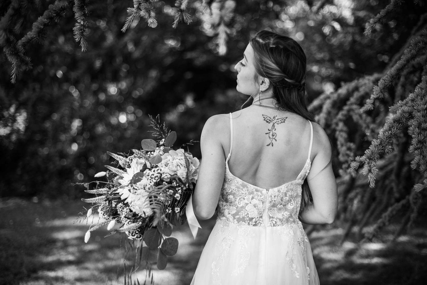 Black and white photo shows intricate lace back detail of wedding dress with bouquet.