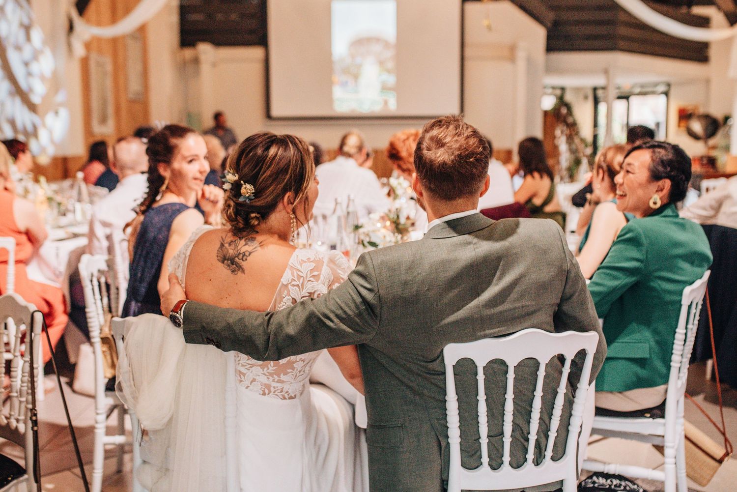 Wedding reception guests seated at elegantly decorated white tables with floral centerpieces.