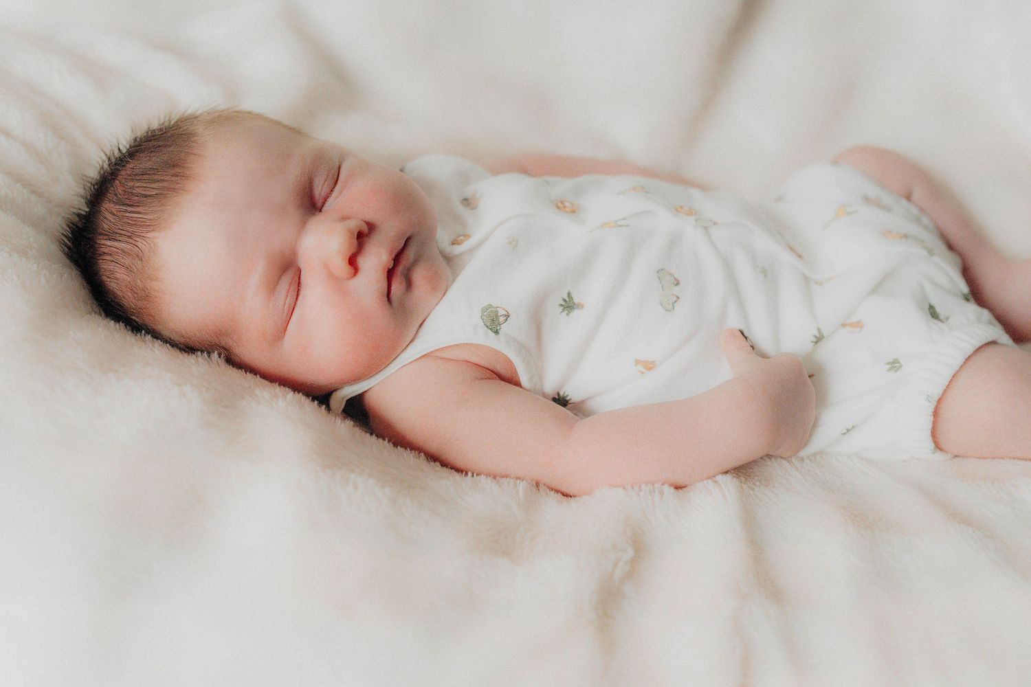 Newborn baby sleeping peacefully on white bedding.