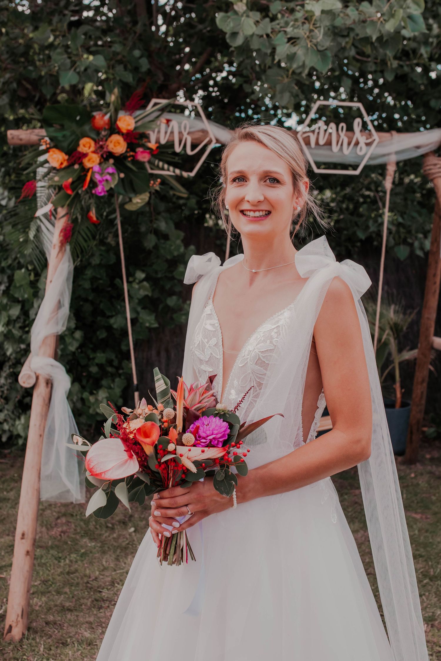 Beautiful wedding ceremony setup with white fabric draped arch and floral decorations in an outdoor garden setting.