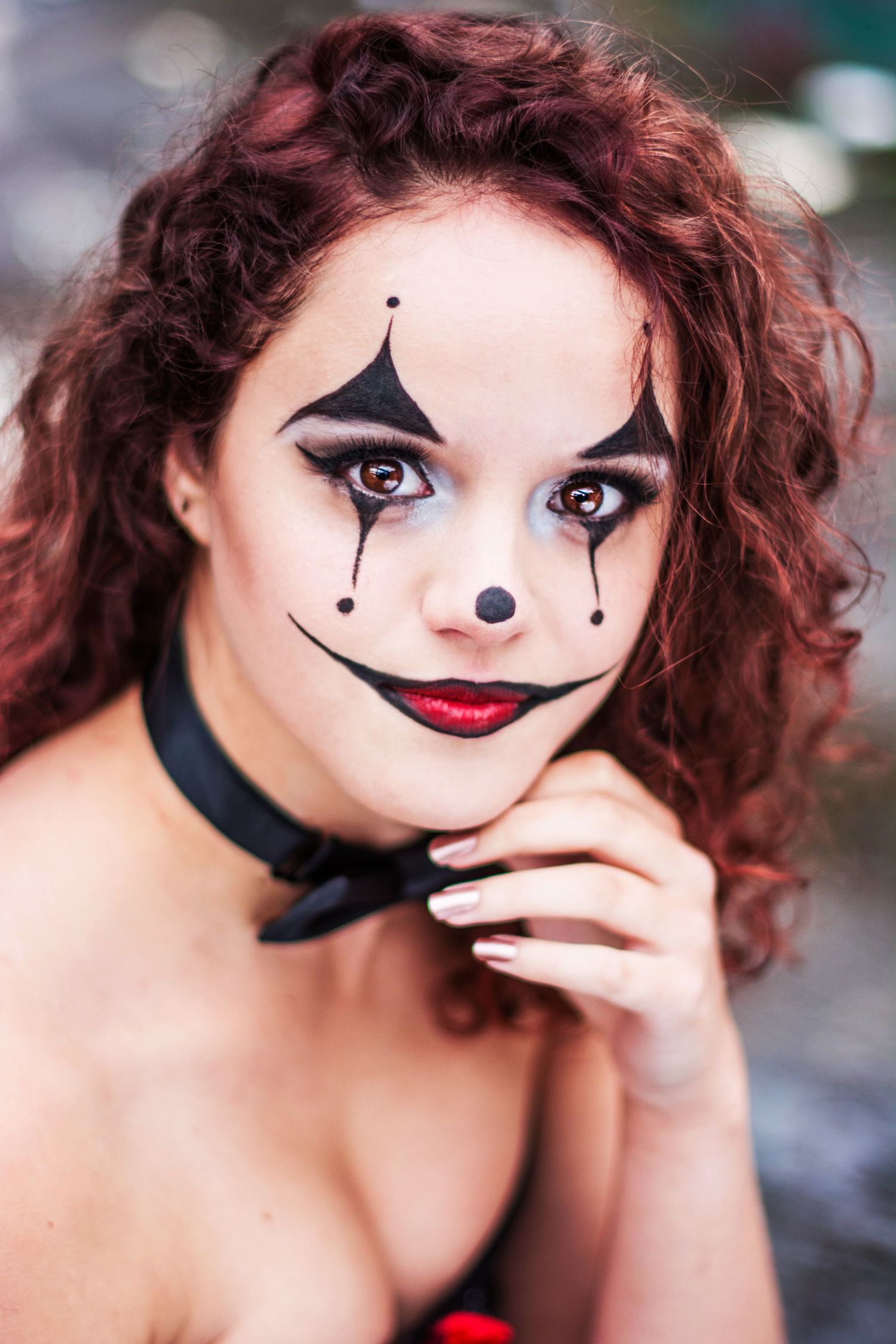 Close-up portrait with dramatic clown-inspired makeup and red curly hair.
