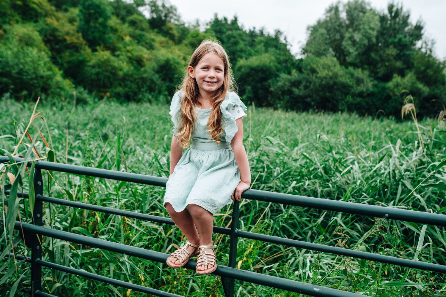 Outdoor photography series showing someone posing near rustic fencing in a grassy field.
