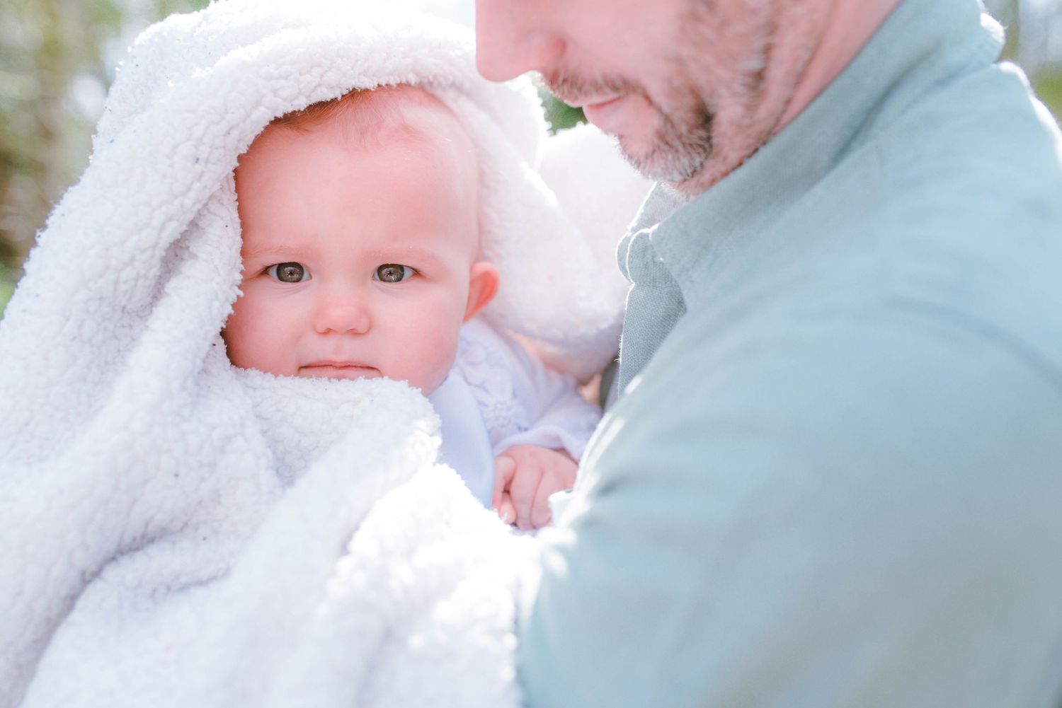 Baby in white baptismal gown photographed outdoors with soft natural lighting.