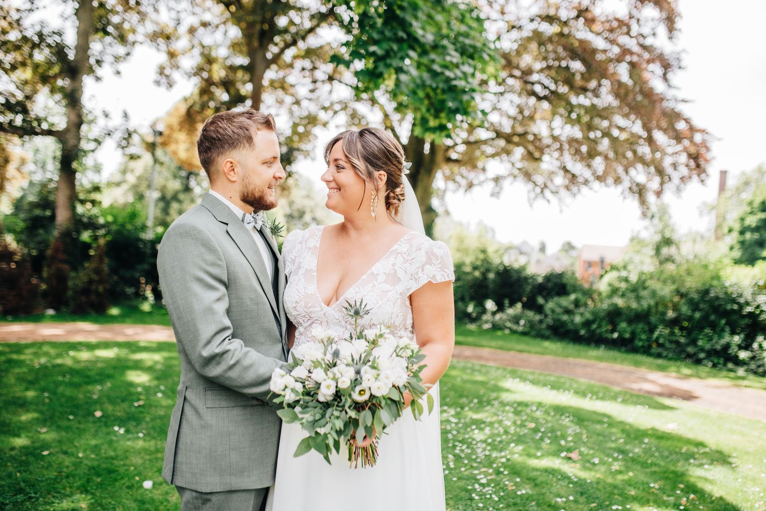 Wedding couple poses together in an outdoor garden setting with elegant white floral bouquet.