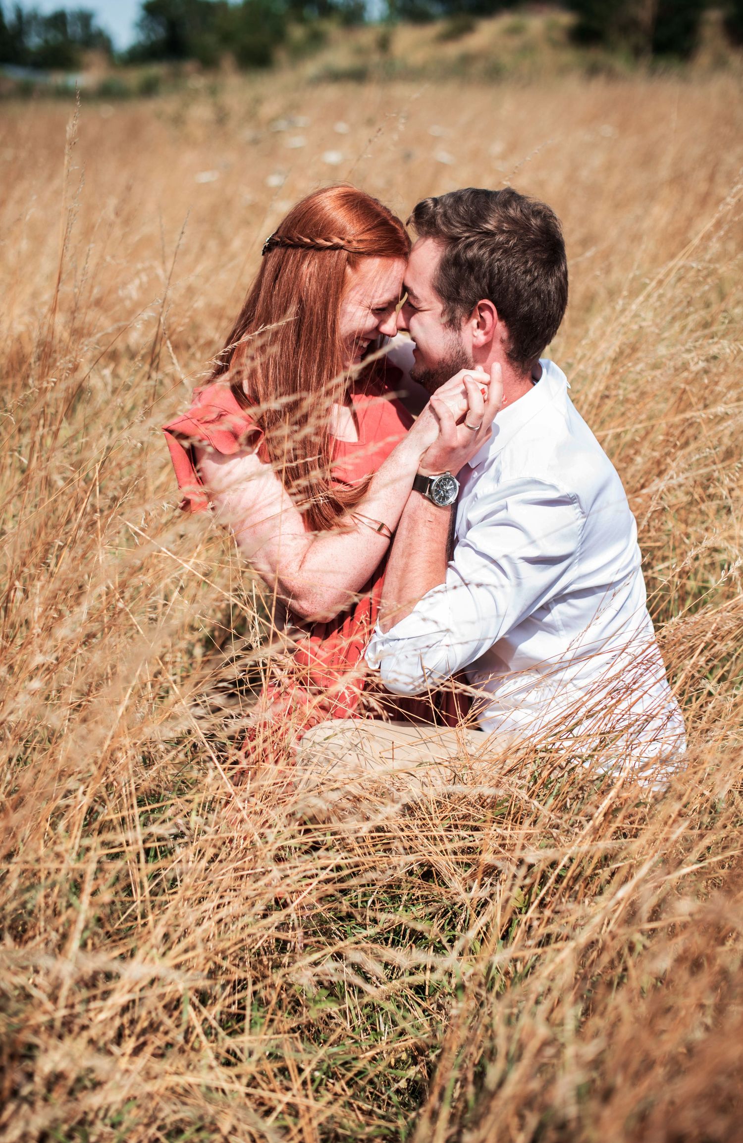 Couple sharing intimate moments while lying in tall golden grass during summer.